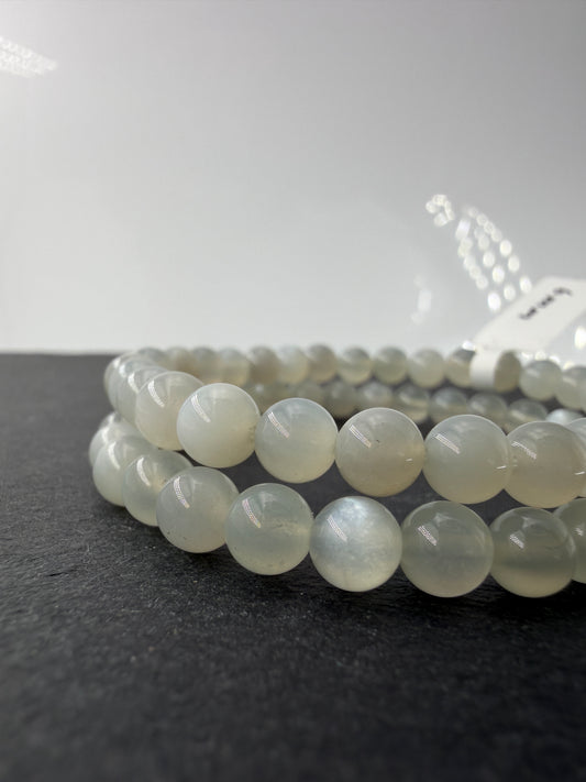 Ein zartes Armband aus glatt polierten, weißen Mondsteinperlen, die auf einem elastischen Band gereiht sind und einen seidigen Schimmer auf der Oberfläche zeigen.
