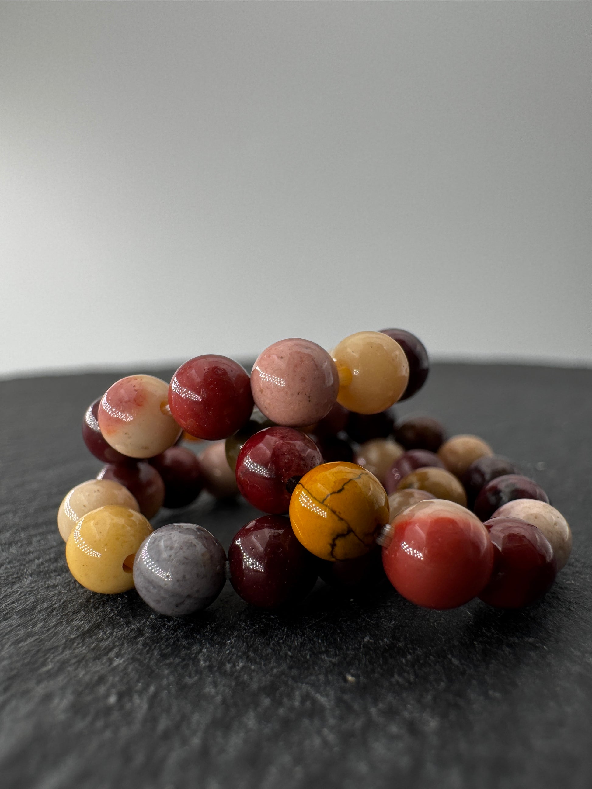 Elastischer Ring aus Mookait mit 4,6-mm-Kugeln – warme Erdtöne in Ocker, Bordeaux und Creme, Ringdurchmesser 5,5–6 cm.
