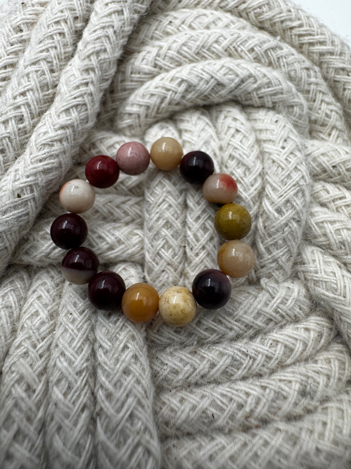 Elastischer Ring aus Mookait mit 4,6-mm-Kugeln – warme Erdtöne in Ocker, Bordeaux und Creme, Ringdurchmesser 5,5–6 cm.
