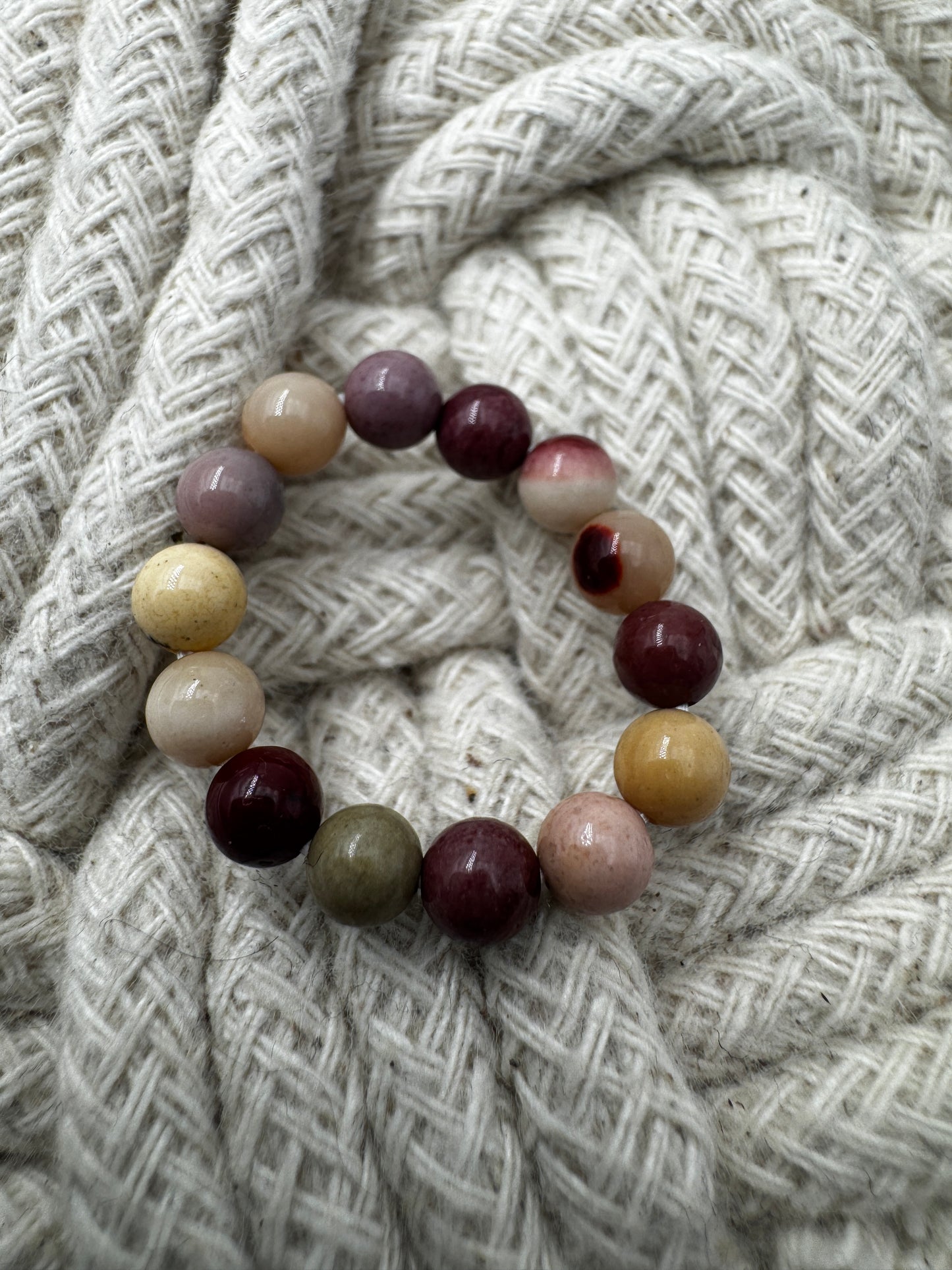 Elastischer Ring aus Mookait mit 4,6-mm-Kugeln – warme Erdtöne in Ocker, Bordeaux und Creme, Ringdurchmesser 5,5–6 cm.