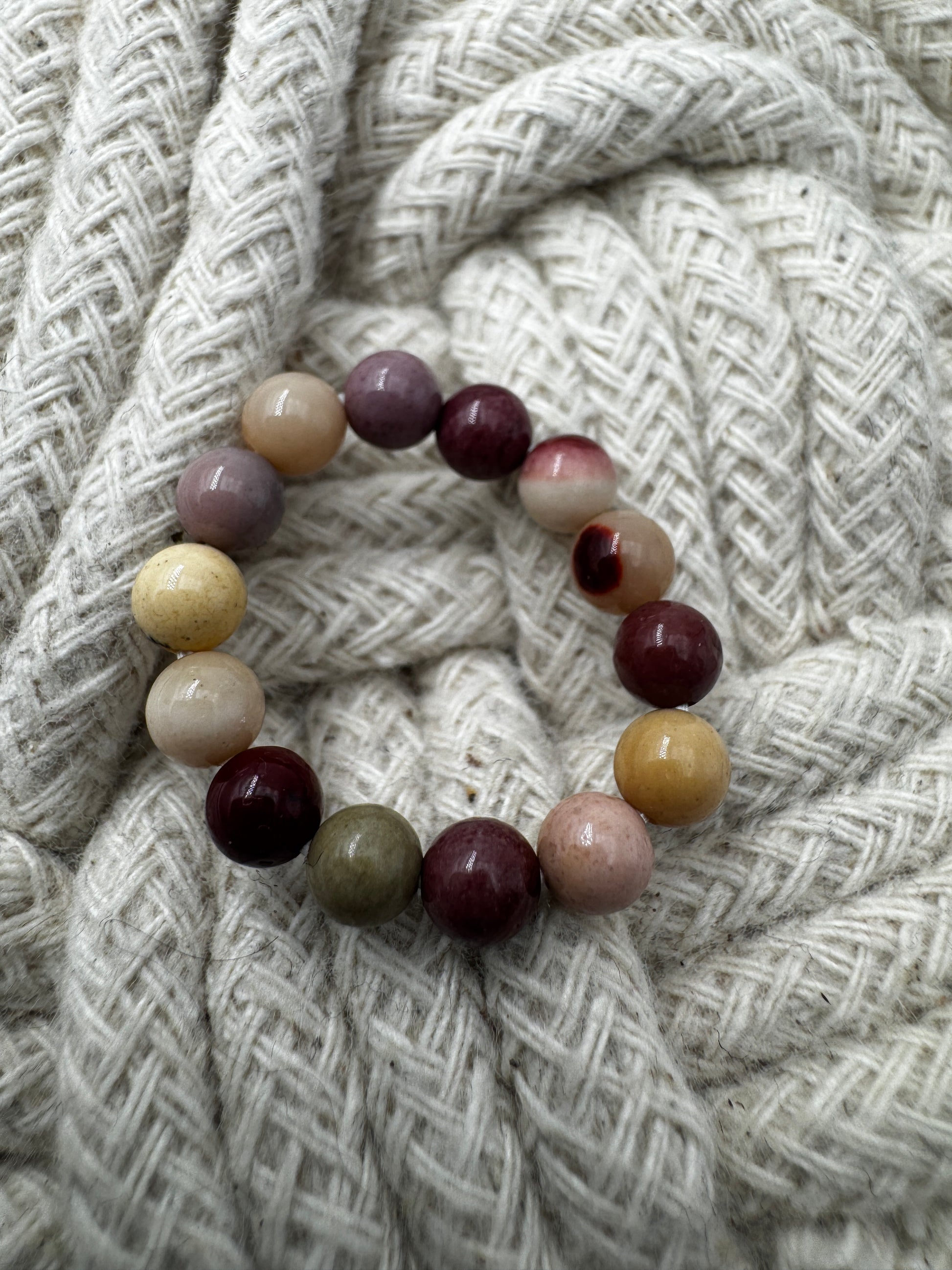 Elastischer Ring aus Mookait mit 4,6-mm-Kugeln – warme Erdtöne in Ocker, Bordeaux und Creme, Ringdurchmesser 5,5–6 cm.