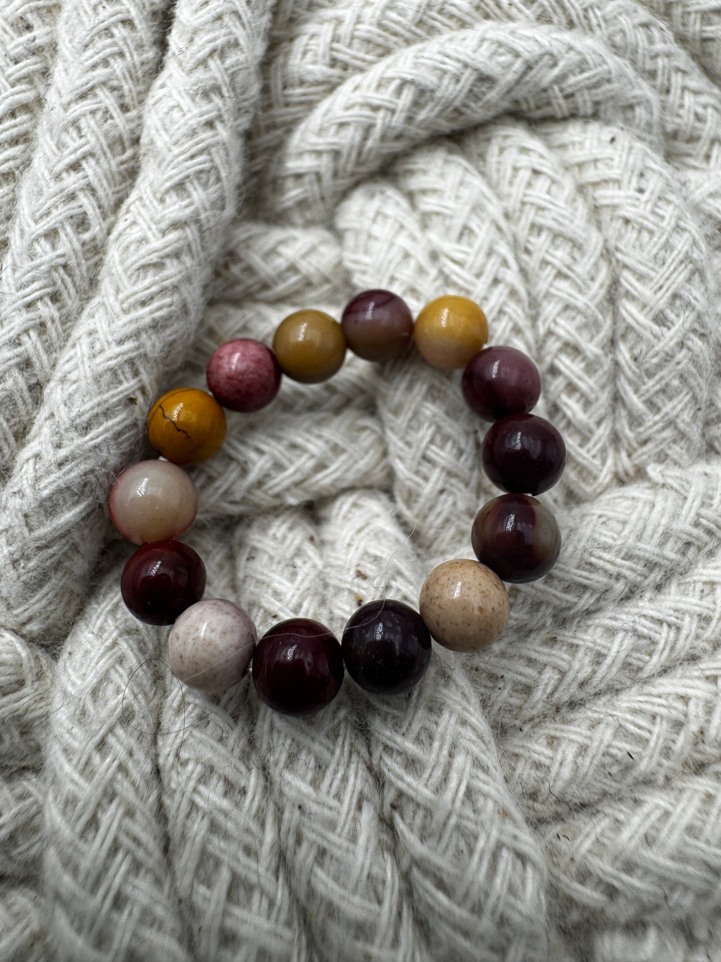Elastischer Ring aus Mookait mit 4,6-mm-Kugeln – warme Erdtöne in Ocker, Bordeaux und Creme, Ringdurchmesser 5,5–6 cm.