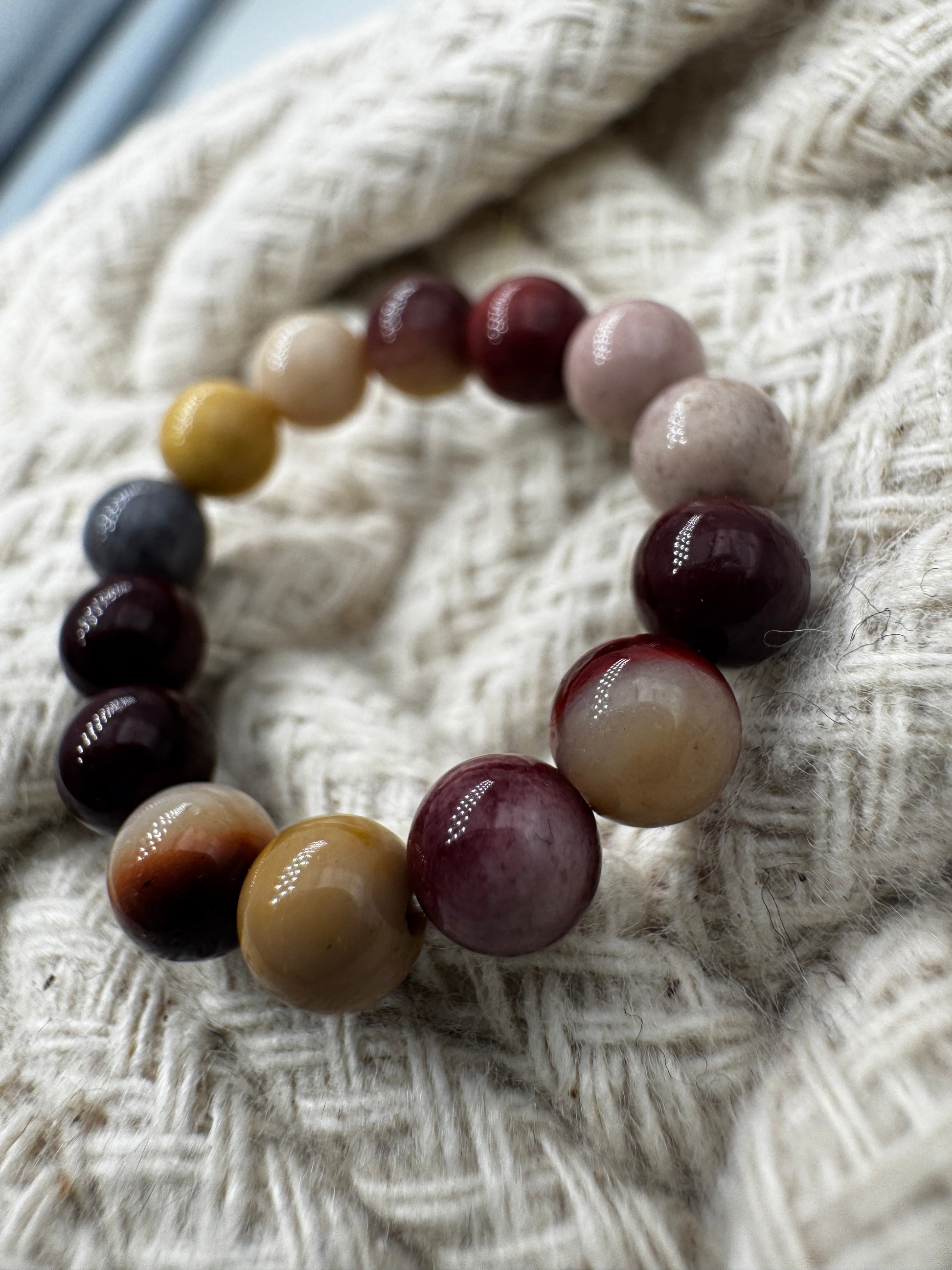 Elastischer Ring aus Mookait mit 4,6-mm-Kugeln – warme Erdtöne in Ocker, Bordeaux und Creme, Ringdurchmesser 5,5–6 cm.