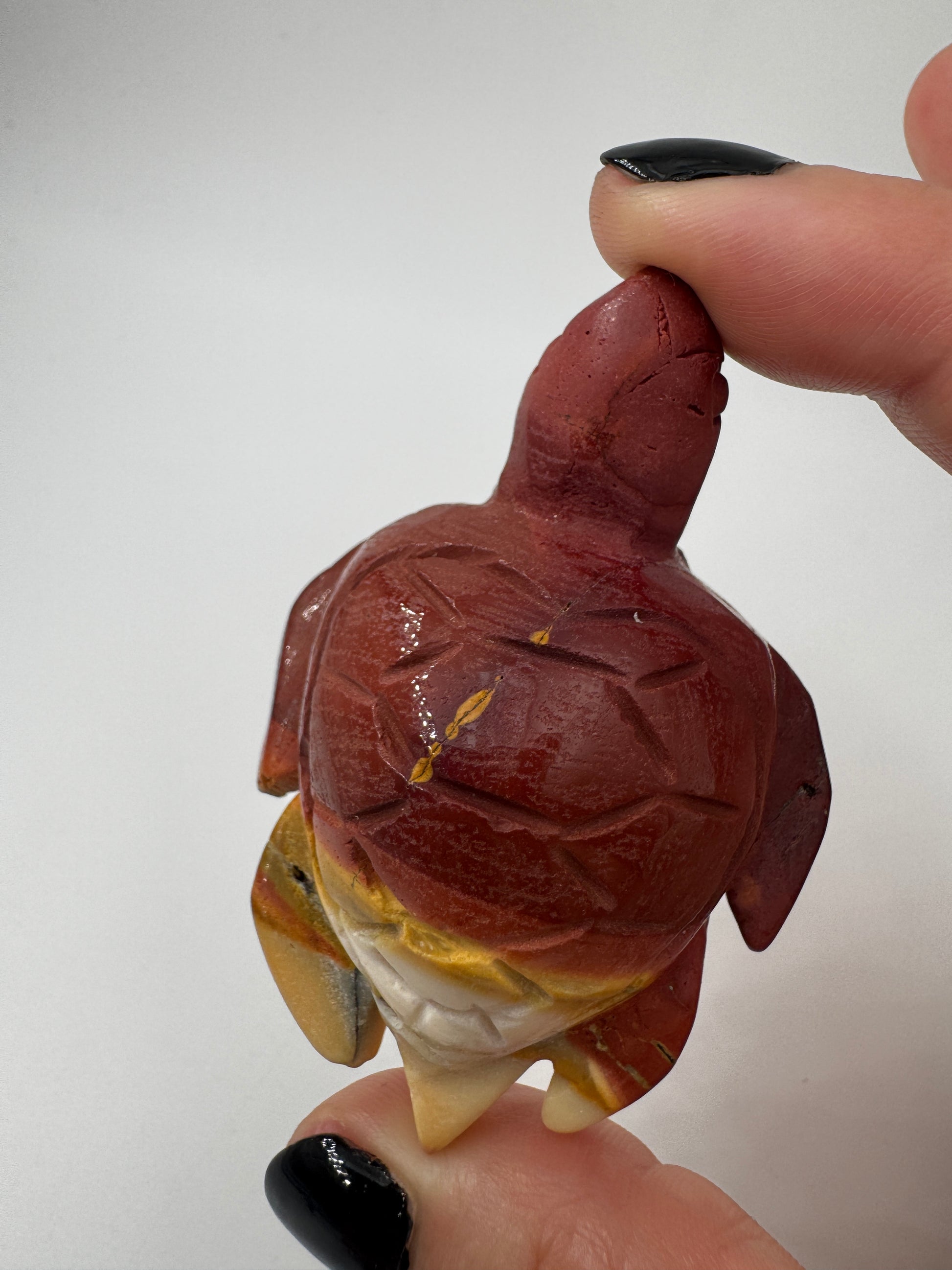 Eine handgeschliffene Schildkröte aus Mookait mit einem kontrastreichen Muster aus gelben und roten Farbfeldern.