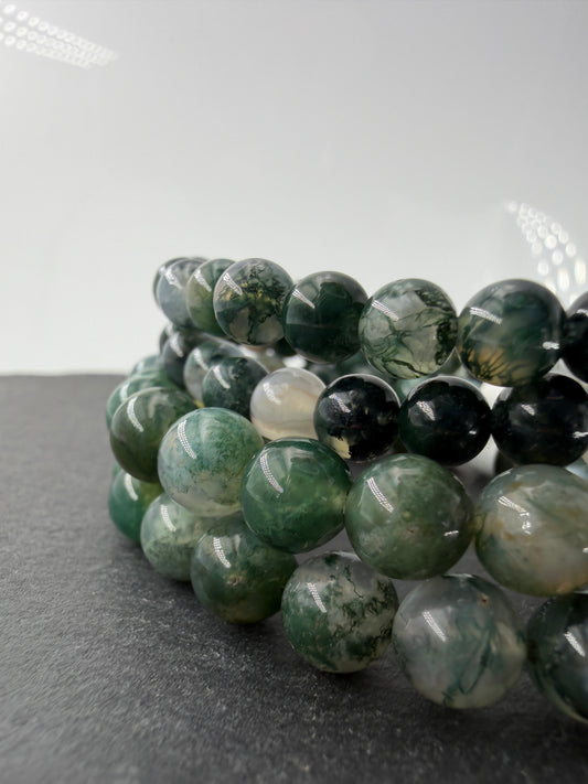 Ein hochwertiges Kugelarmband aus Moosachat, dessen einzelne Perlen klare bis weißliche Partien mit tiefgrünen Mineraleinschlüssen kombinieren.