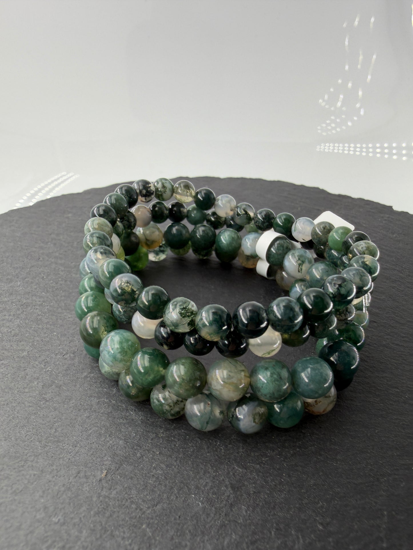 Ein hochwertiges Kugelarmband aus Moosachat, dessen einzelne Perlen klare bis weißliche Partien mit tiefgrünen Mineraleinschlüssen kombinieren.