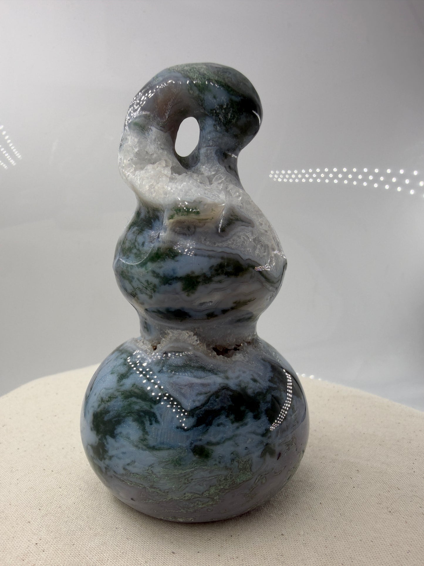 Eine polierte Skulptur in Form eines Flaschenkürbisses aus Moosachat mit tiefgrünen, moosartigen Strukturen in einer milchig-transparenten Matrix.