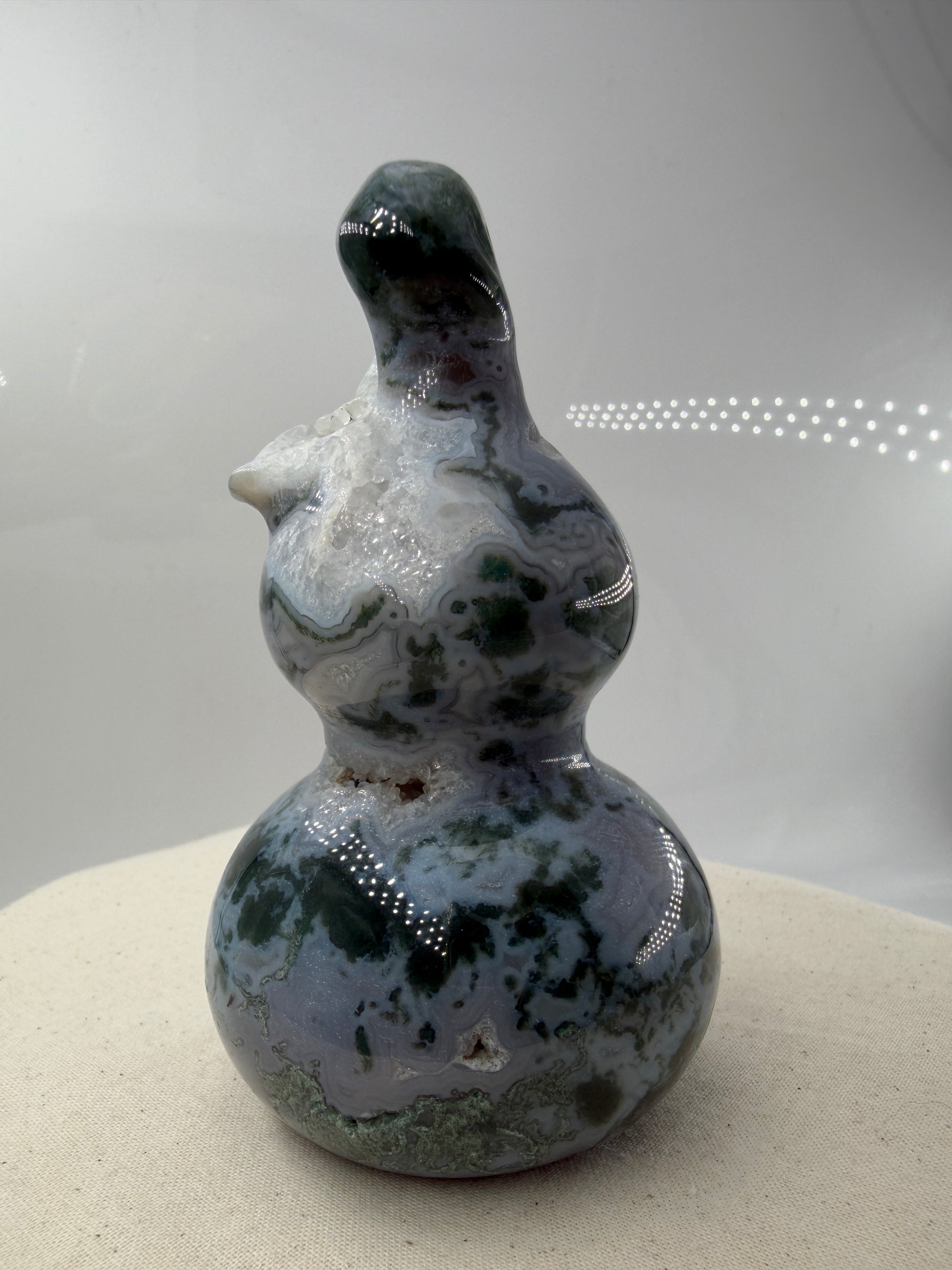 Eine polierte Skulptur in Form eines Flaschenkürbisses aus Moosachat mit tiefgrünen, moosartigen Strukturen in einer milchig-transparenten Matrix.