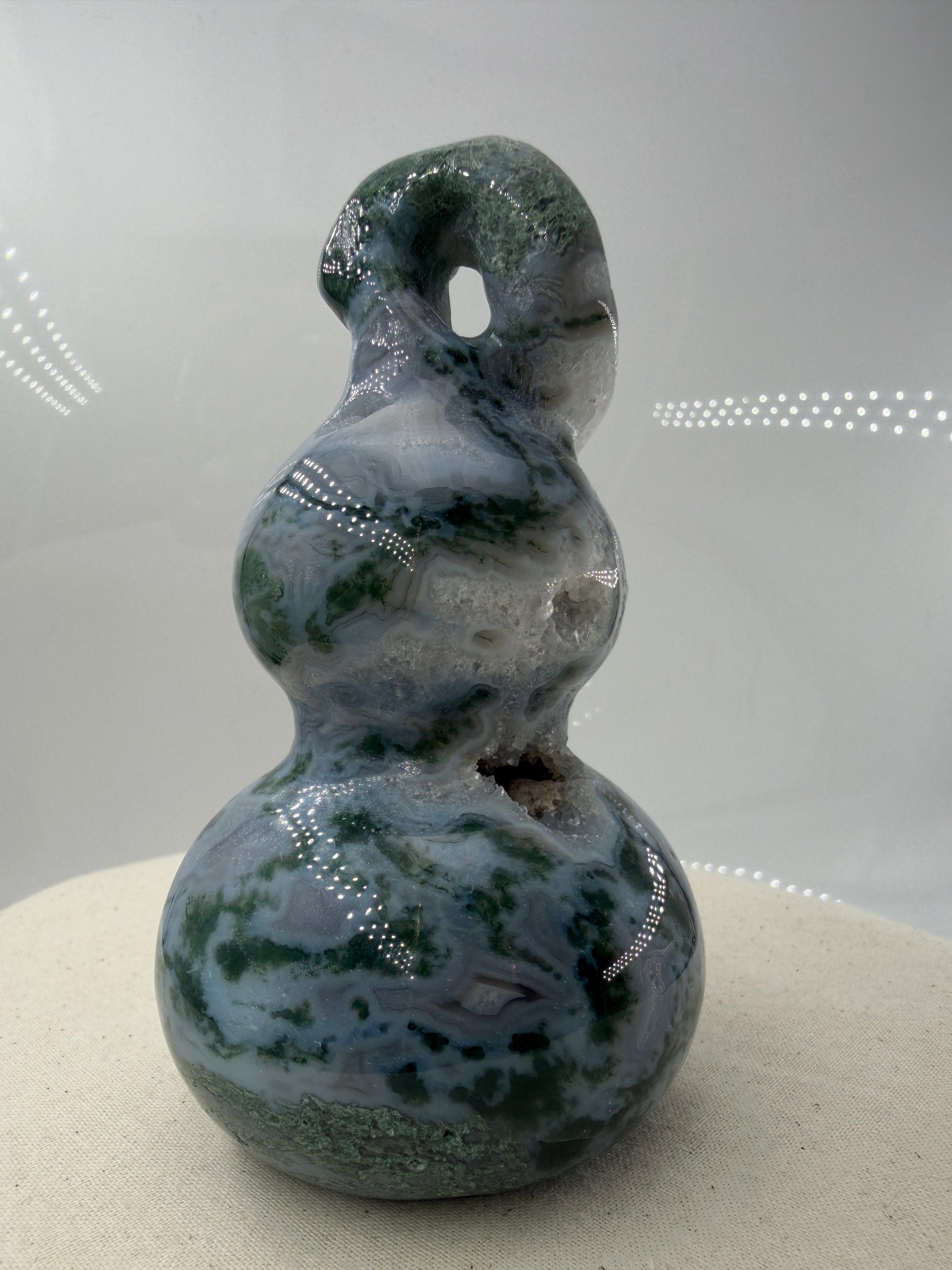 Eine polierte Skulptur in Form eines Flaschenkürbisses aus Moosachat mit tiefgrünen, moosartigen Strukturen in einer milchig-transparenten Matrix.