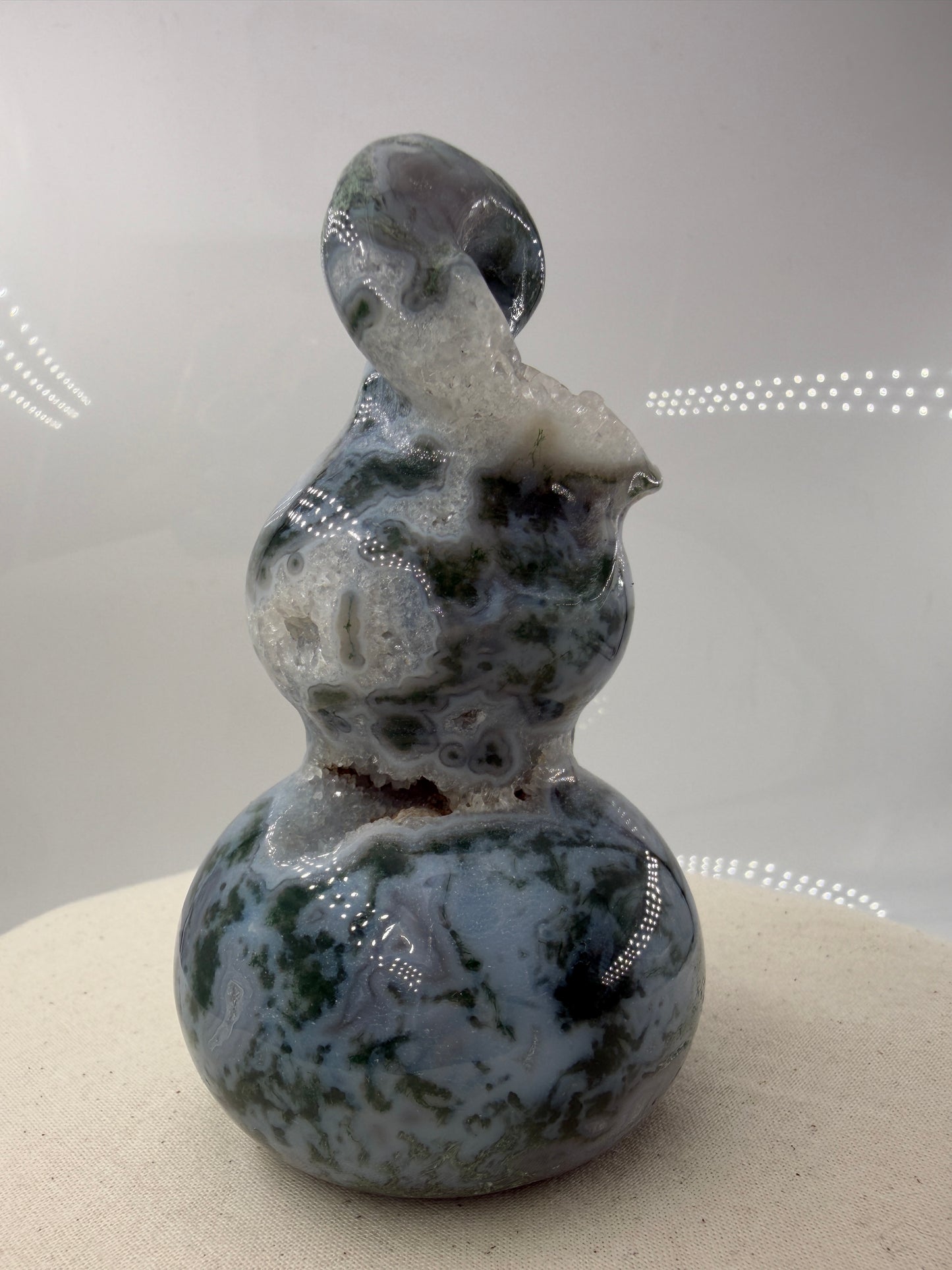 Eine polierte Skulptur in Form eines Flaschenkürbisses aus Moosachat mit tiefgrünen, moosartigen Strukturen in einer milchig-transparenten Matrix.