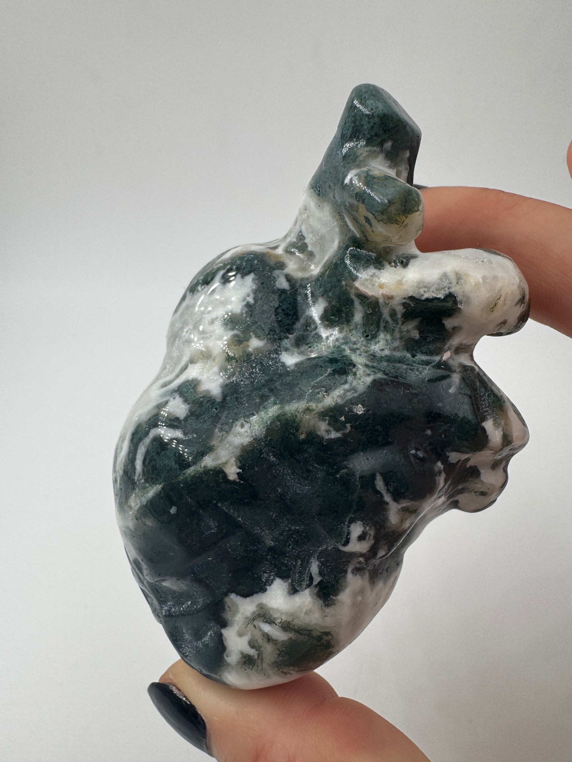 Ein anatomisch geformtes Herz aus Moosachat mit moosgrünen Einschlüssen in einer milchig-weißen Matrix und fein polierter Oberfläche.