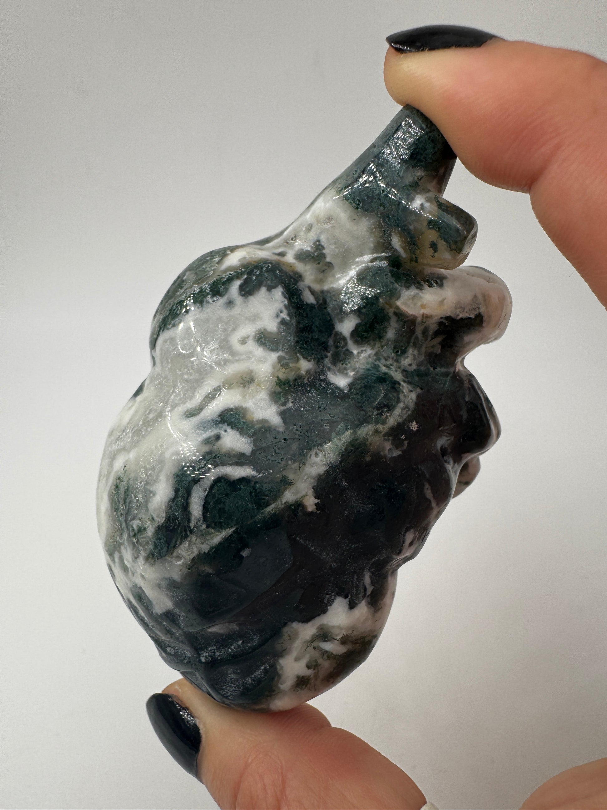 Ein anatomisch geformtes Herz aus Moosachat mit moosgrünen Einschlüssen in einer milchig-weißen Matrix und fein polierter Oberfläche.