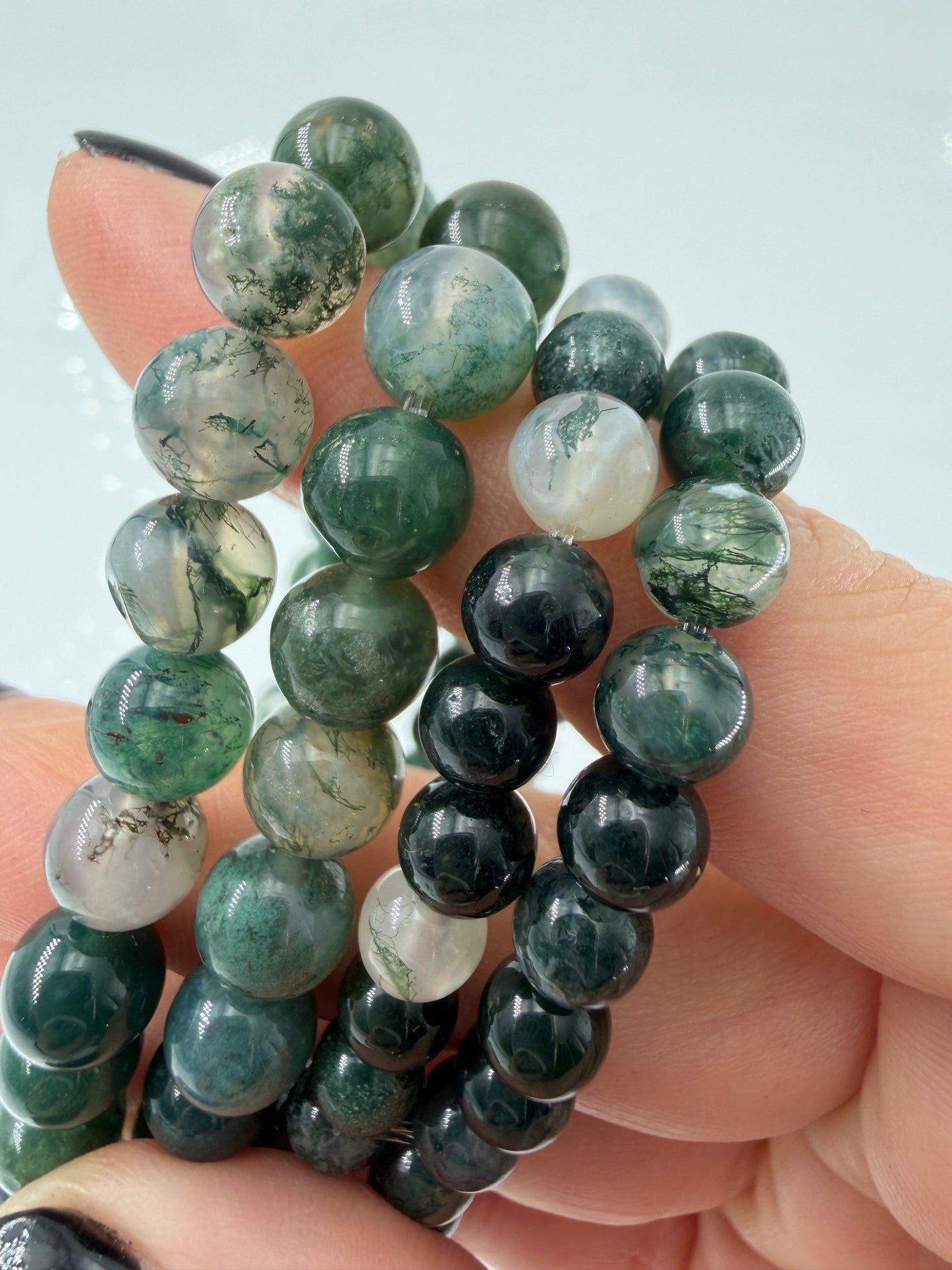 Ein hochwertiges Kugelarmband aus Moosachat, dessen einzelne Perlen klare bis weißliche Partien mit tiefgrünen Mineraleinschlüssen kombinieren.