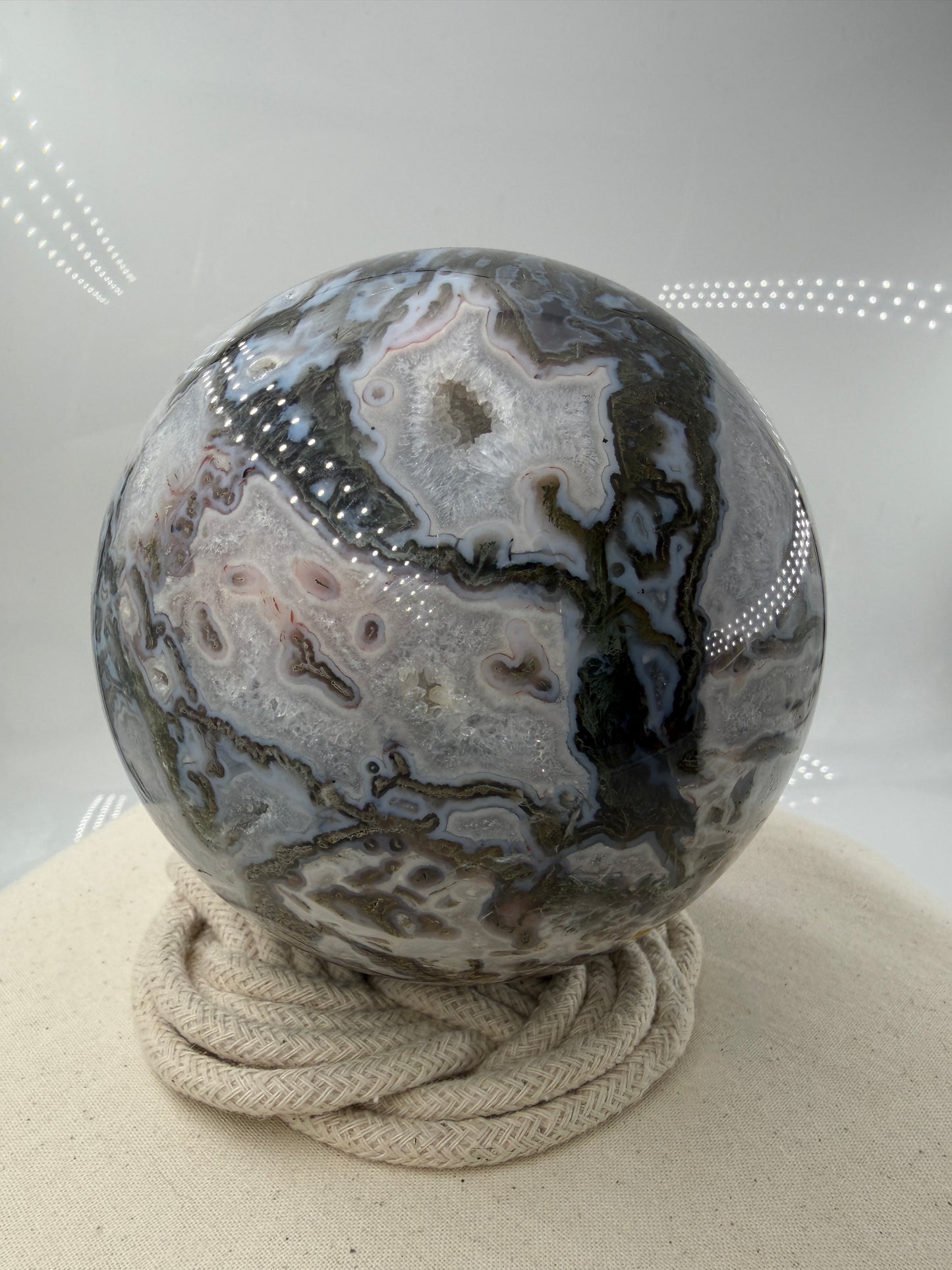 Eine hochglanzpolierte Moosachat-Kugel mit tiefgrünen, pflanzenähnlichen Strukturen in einer teils transparenten Matrix.