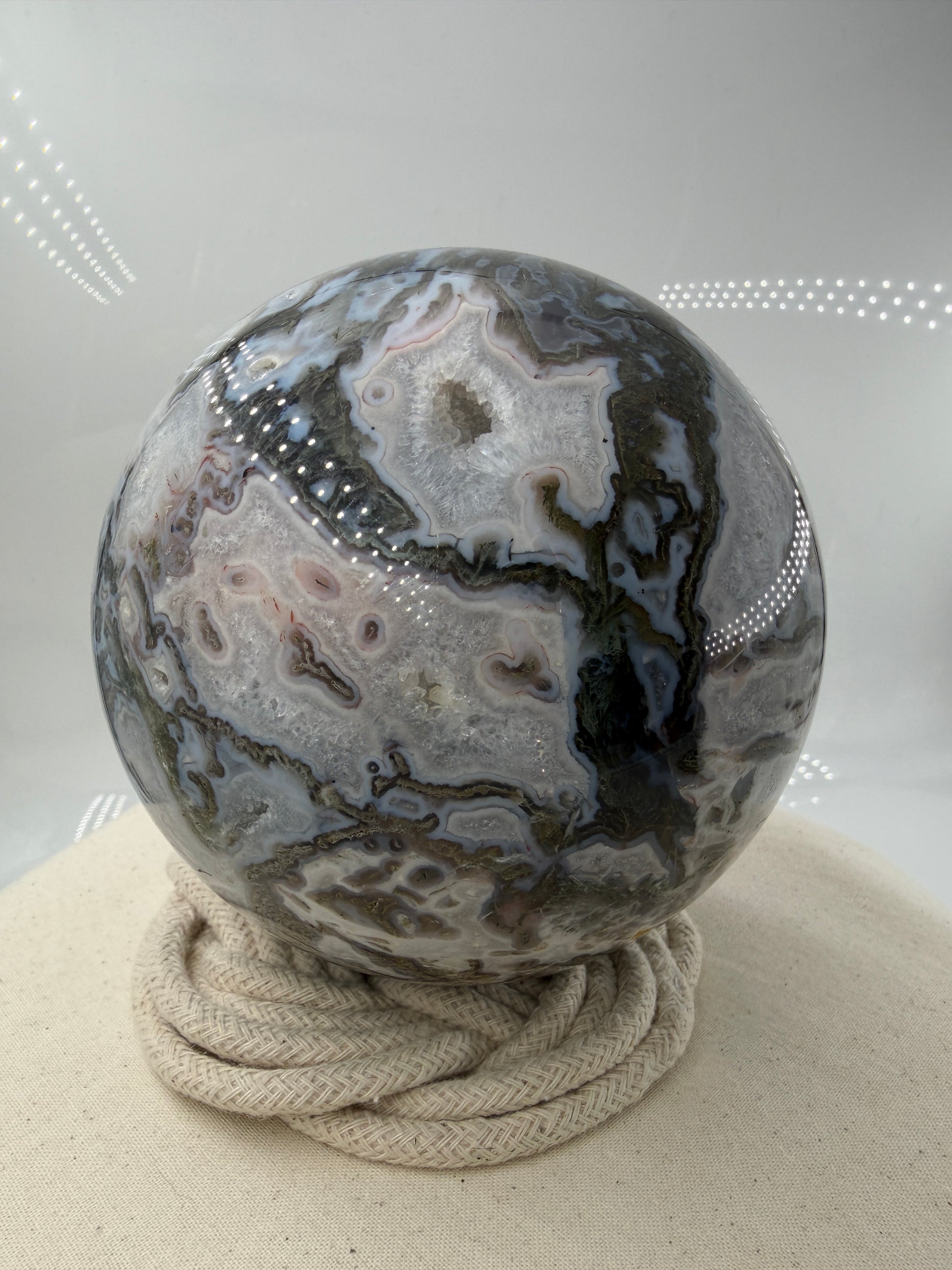 Eine hochglanzpolierte Moosachat-Kugel mit tiefgrünen, pflanzenähnlichen Strukturen in einer teils transparenten Matrix.