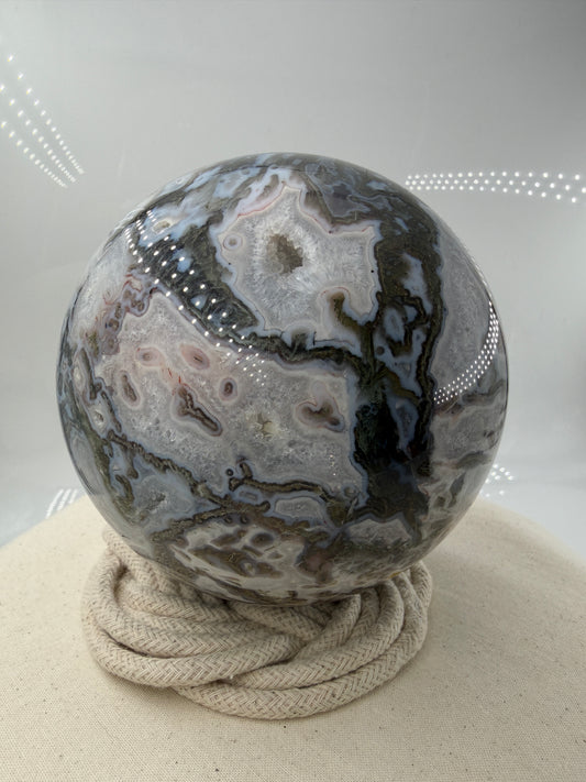 Eine hochglanzpolierte Moosachat-Kugel mit tiefgrünen, pflanzenähnlichen Strukturen in einer teils transparenten Matrix.