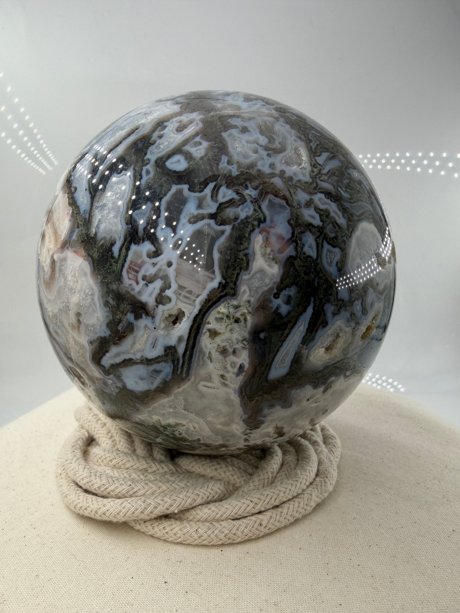 Eine hochglanzpolierte Moosachat-Kugel mit tiefgrünen, pflanzenähnlichen Strukturen in einer teils transparenten Matrix.