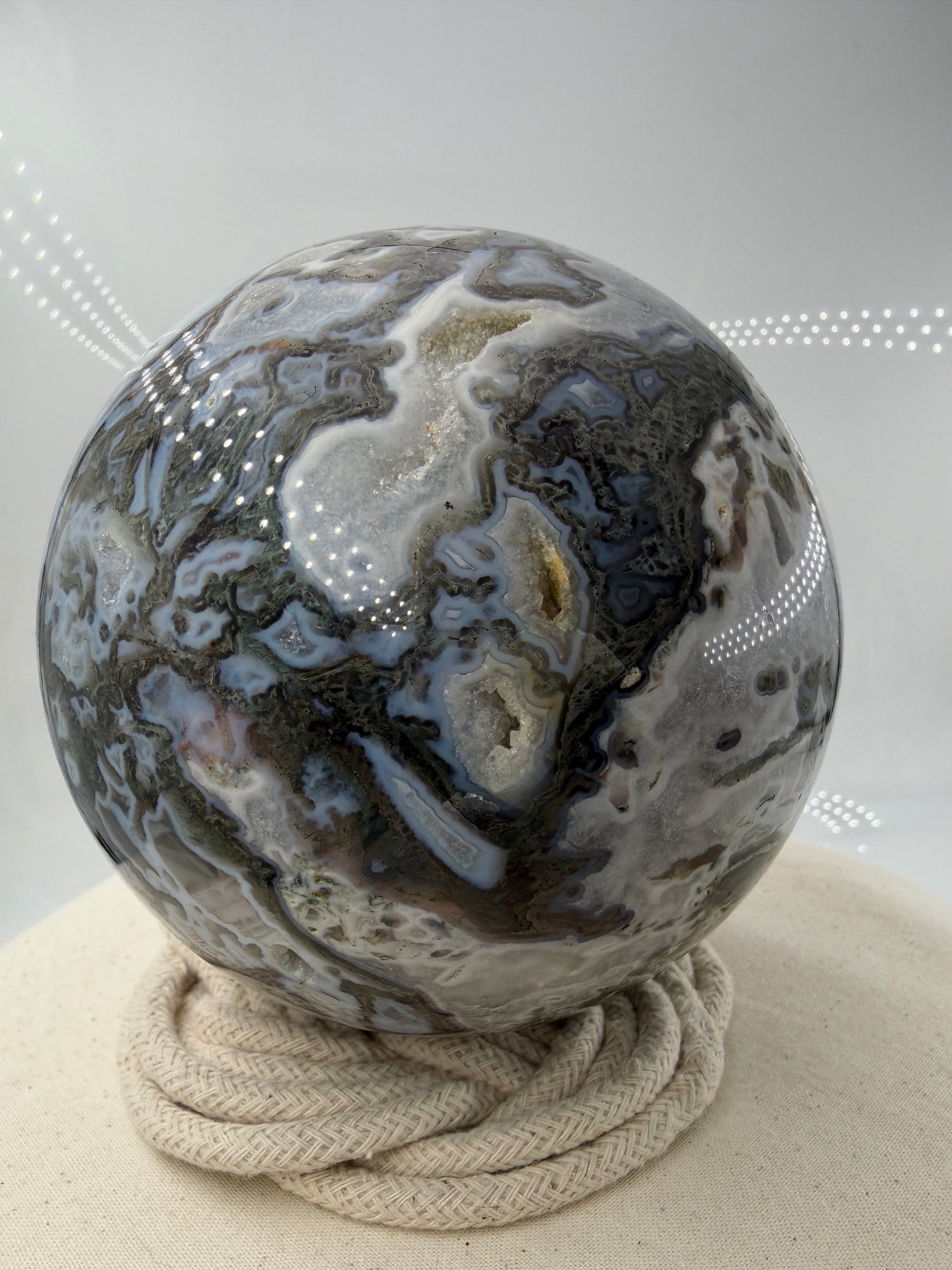 Eine hochglanzpolierte Moosachat-Kugel mit tiefgrünen, pflanzenähnlichen Strukturen in einer teils transparenten Matrix.