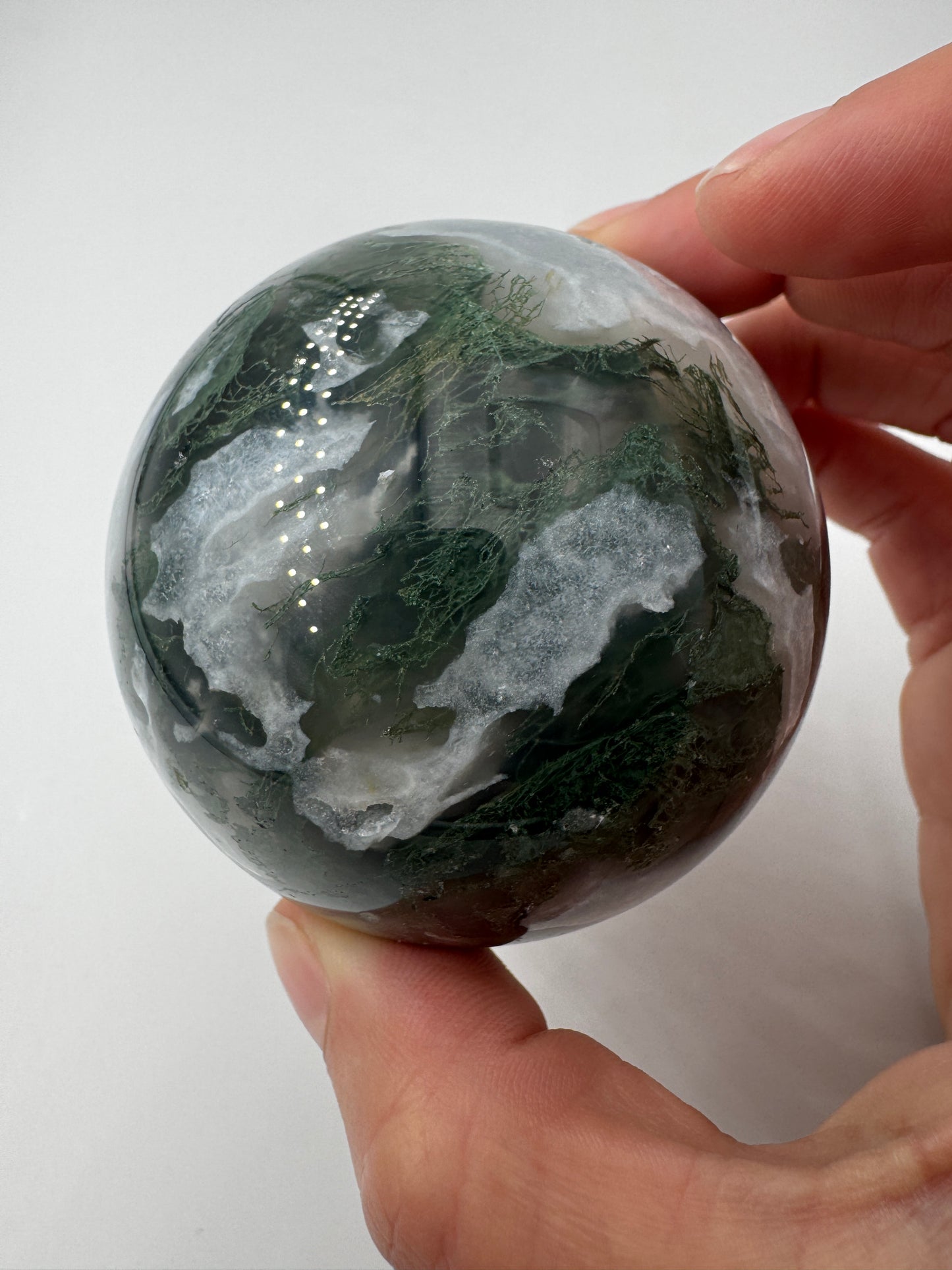 Eine hochglanzpolierte Moosachat-Kugel mit tiefgrünen, pflanzenähnlichen Strukturen in einer teils transparenten Matrix.