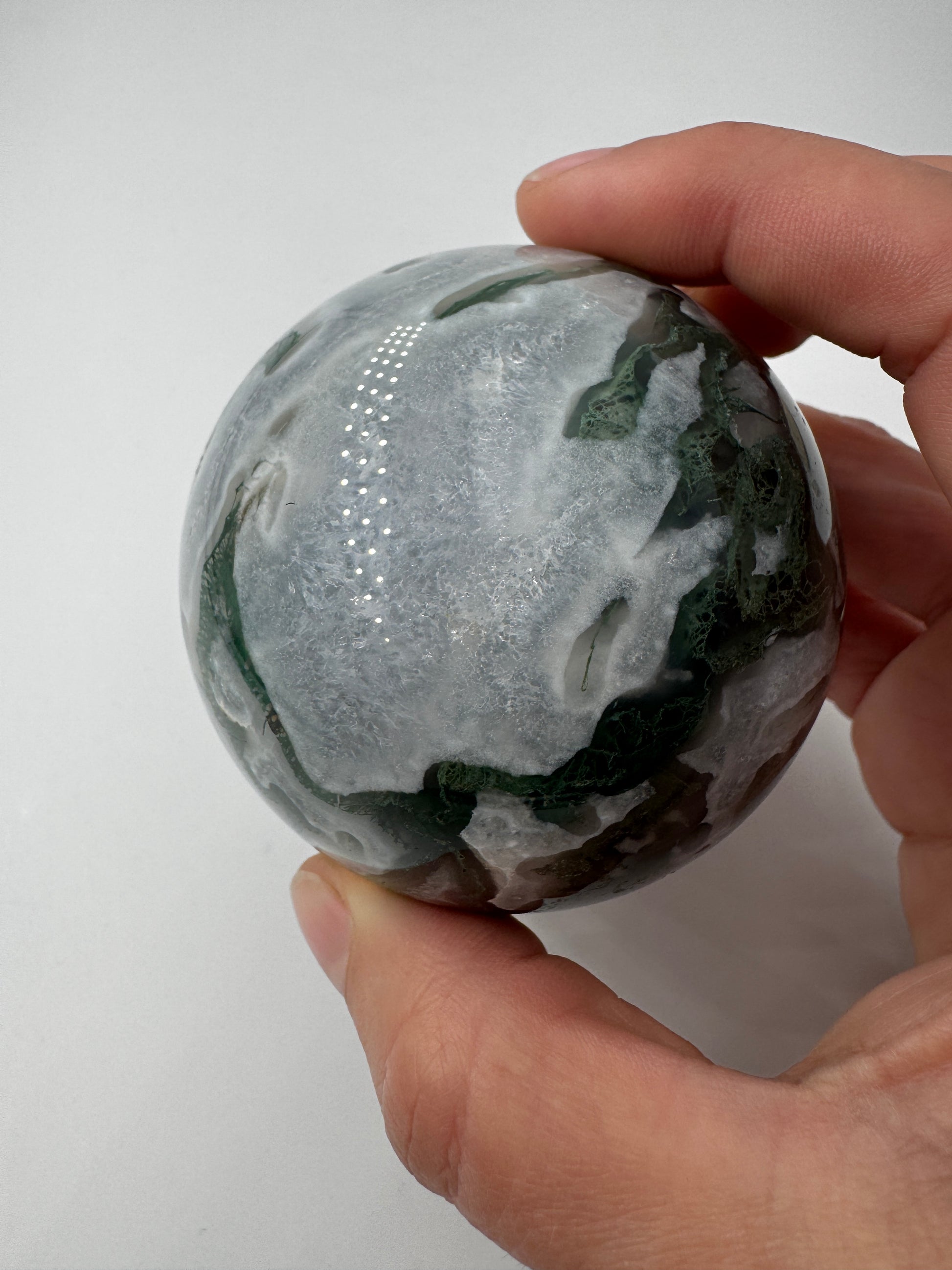 Eine hochglanzpolierte Moosachat-Kugel mit tiefgrünen, pflanzenähnlichen Strukturen in einer teils transparenten Matrix.