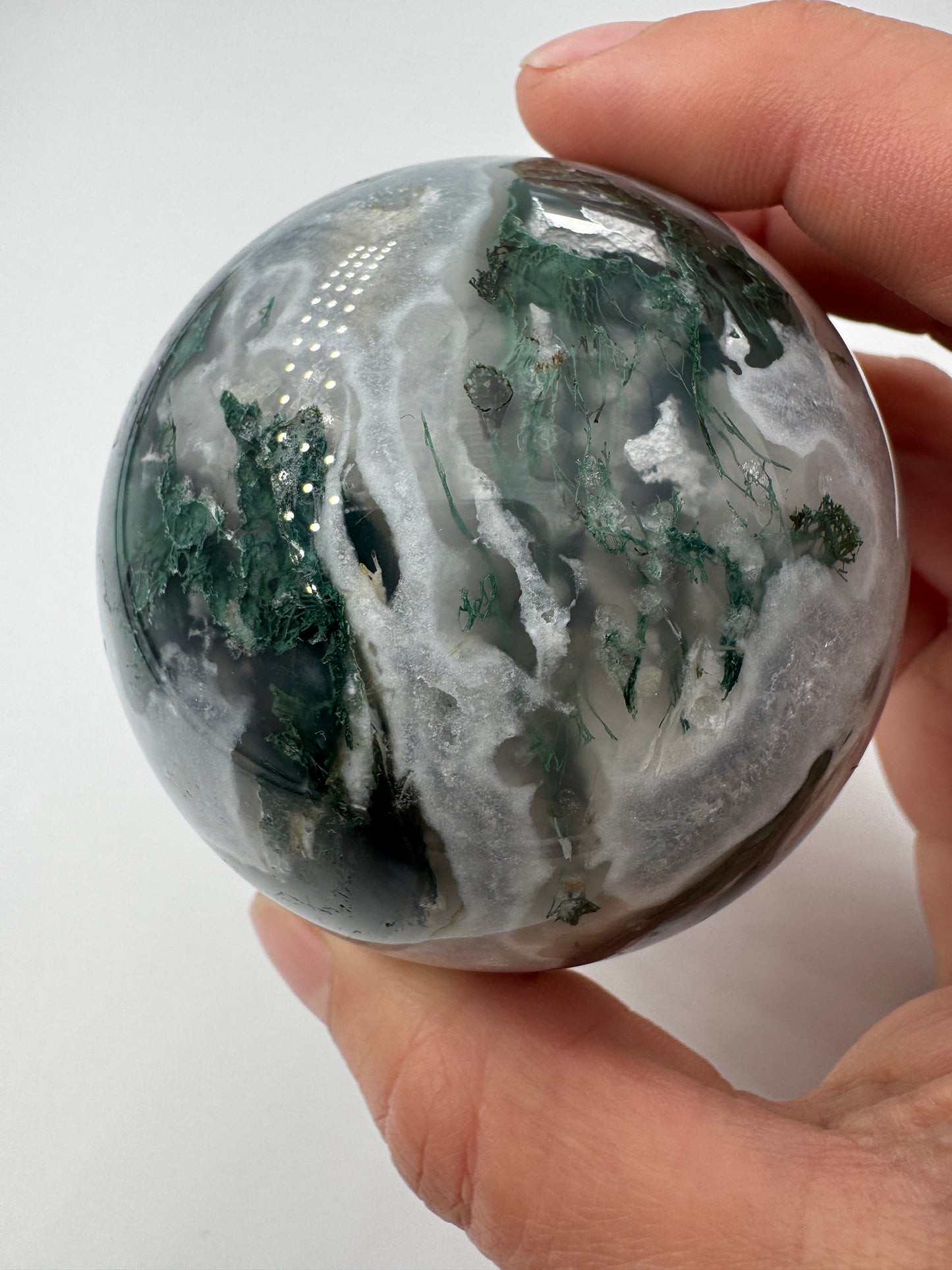 Eine hochglanzpolierte Moosachat-Kugel mit tiefgrünen, pflanzenähnlichen Strukturen in einer teils transparenten Matrix.