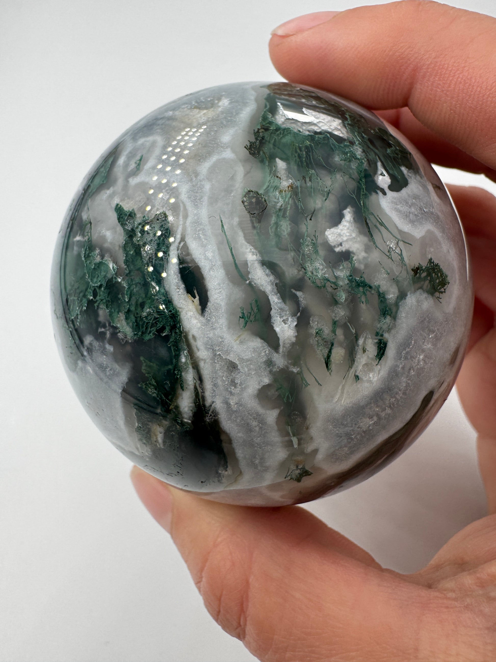 Eine hochglanzpolierte Moosachat-Kugel mit tiefgrünen, pflanzenähnlichen Strukturen in einer teils transparenten Matrix.