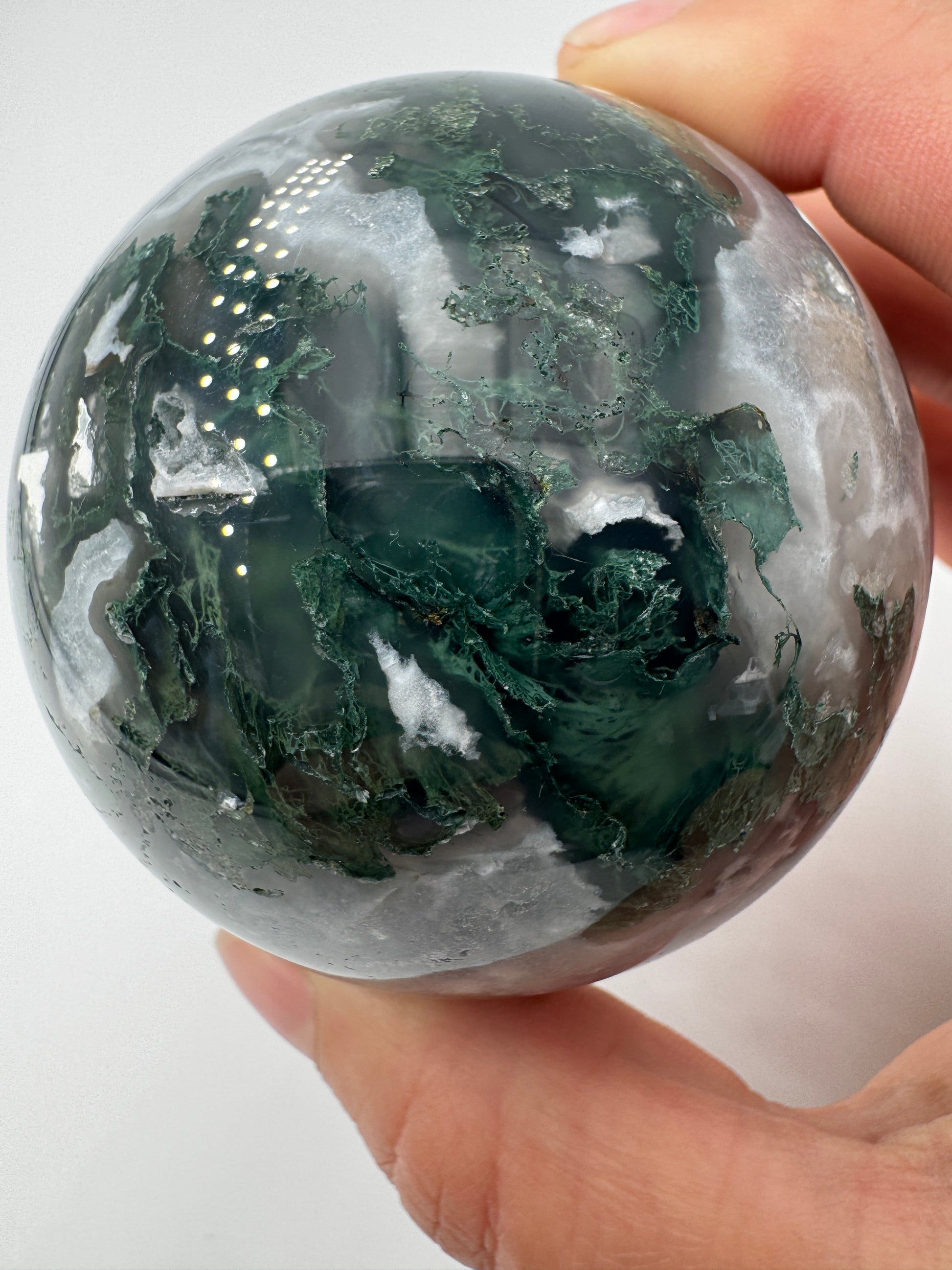 Eine hochglanzpolierte Moosachat-Kugel mit tiefgrünen, pflanzenähnlichen Strukturen in einer teils transparenten Matrix.