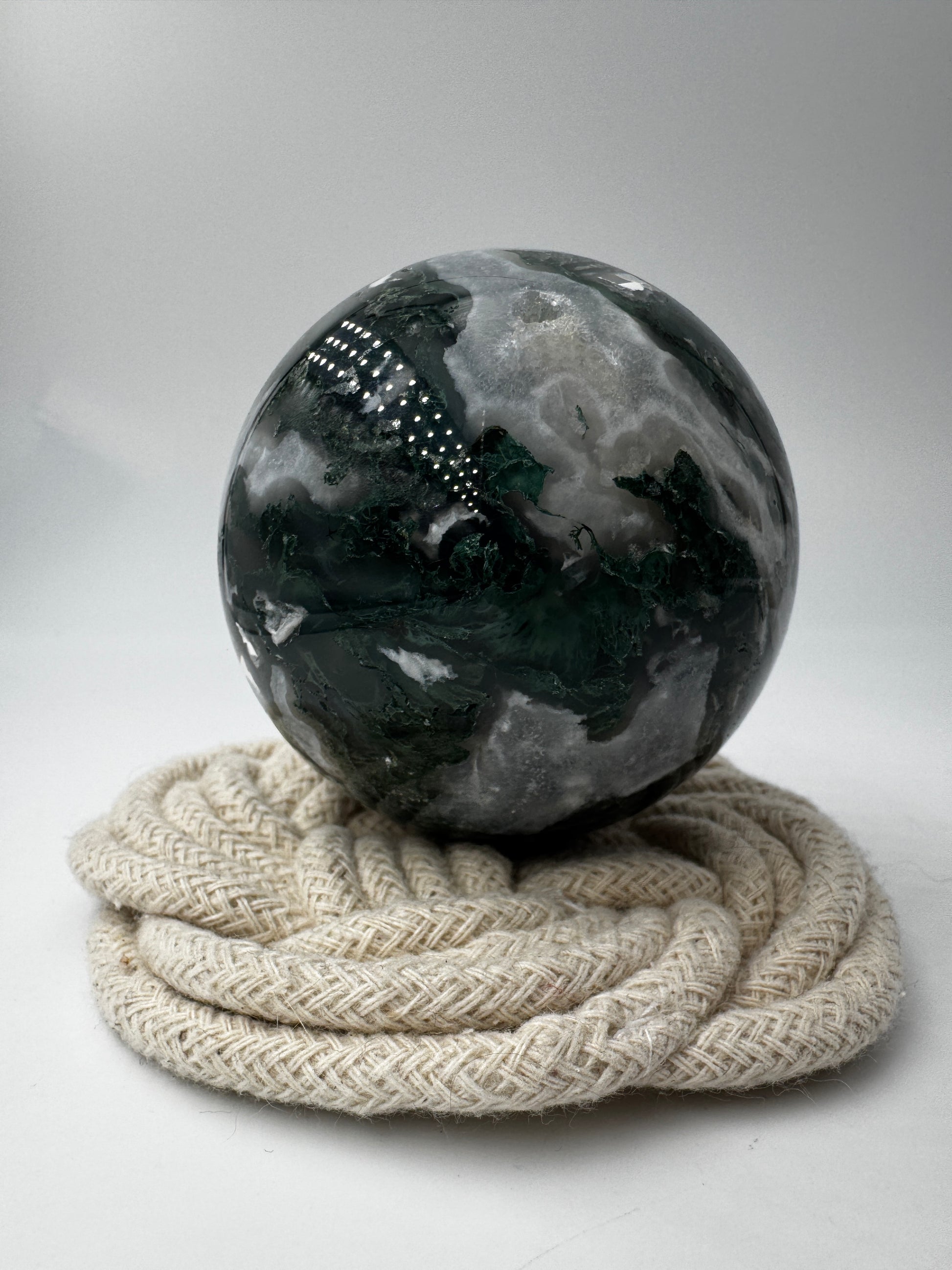 Eine hochglanzpolierte Moosachat-Kugel mit tiefgrünen, pflanzenähnlichen Strukturen in einer teils transparenten Matrix.