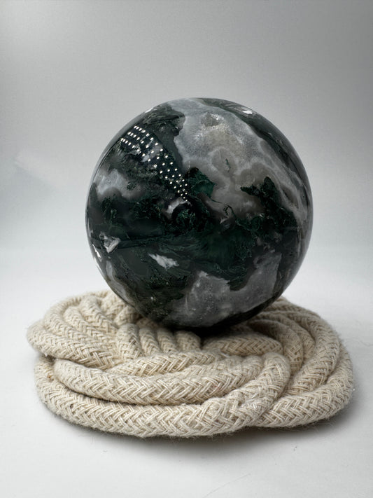Eine hochglanzpolierte Moosachat-Kugel mit tiefgrünen, pflanzenähnlichen Strukturen in einer teils transparenten Matrix.