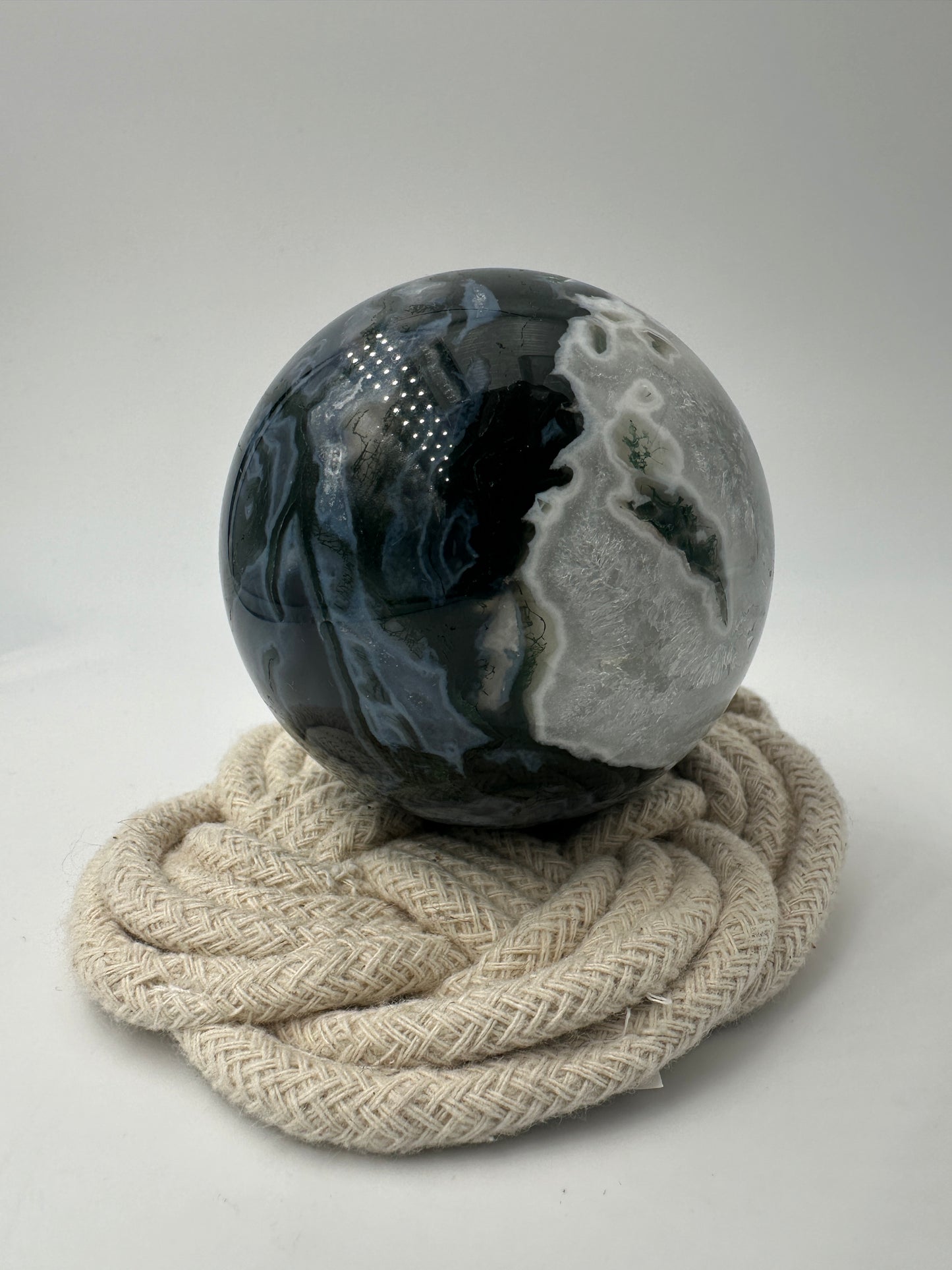 Eine auf hochglanzpolierte Moosachat-Kugel mit tiefgrünen, pflanzenähnlichen Strukturen in einer teils transparenten Matrix.