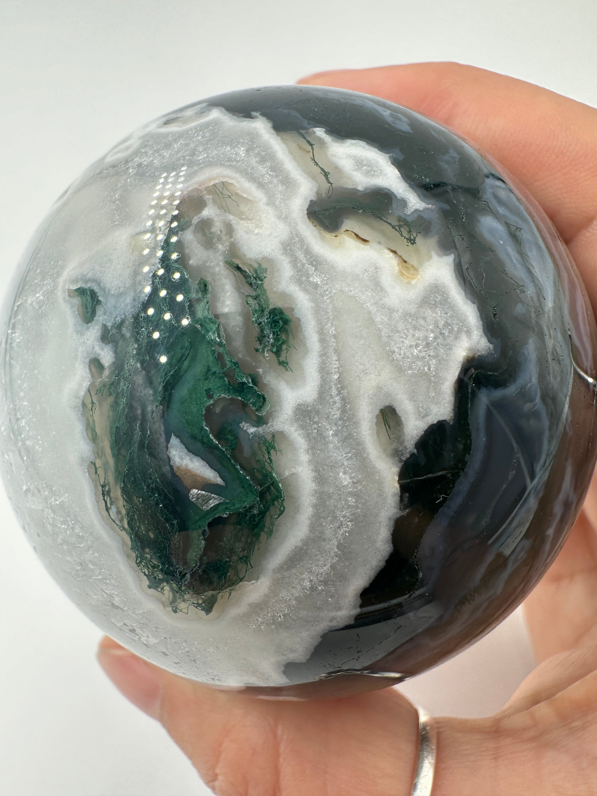 Eine auf hochglanzpolierte Moosachat-Kugel mit tiefgrünen, pflanzenähnlichen Strukturen in einer teils transparenten Matrix.