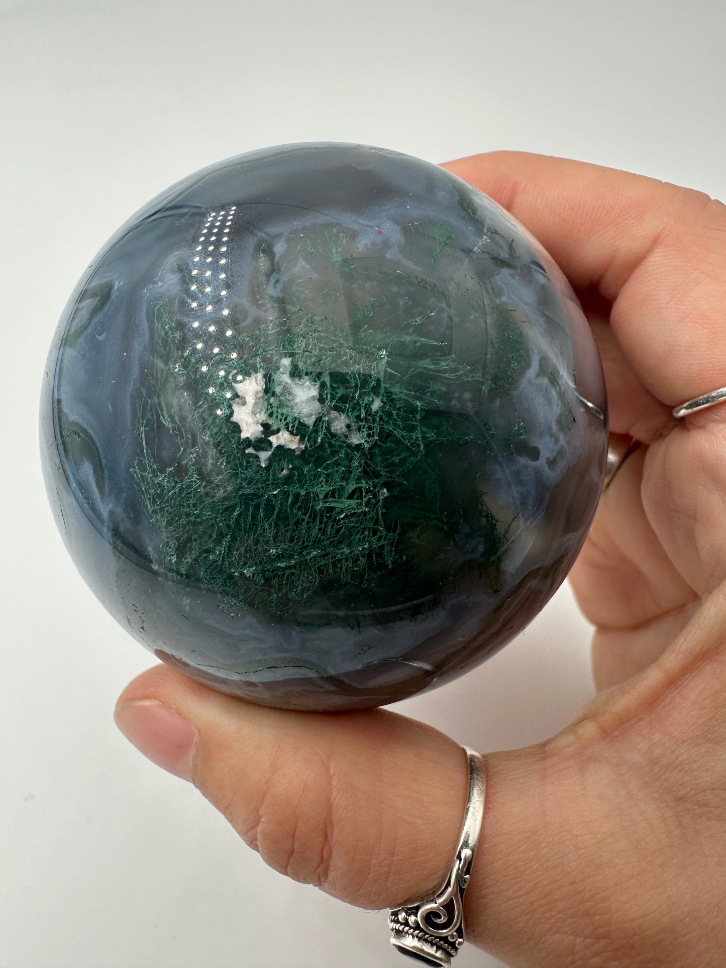 Eine auf hochglanzpolierte Moosachat-Kugel mit tiefgrünen, pflanzenähnlichen Strukturen in einer teils transparenten Matrix.
