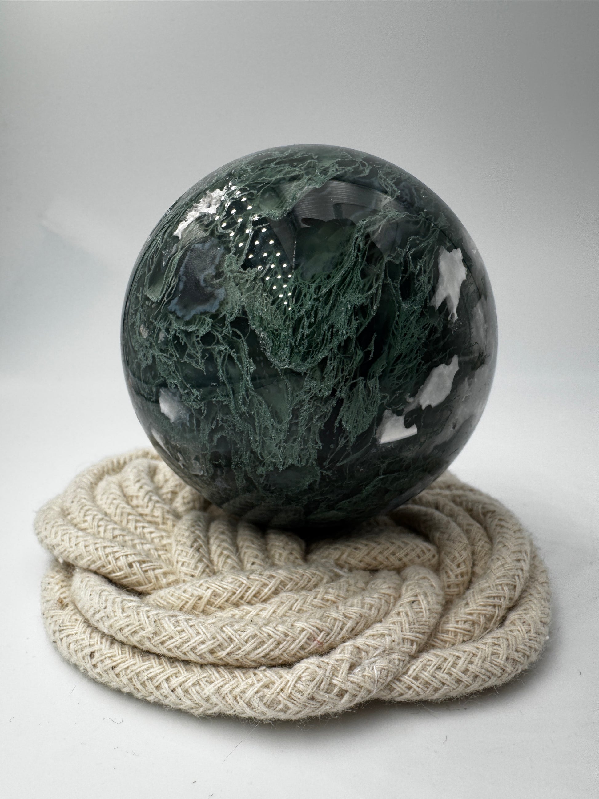 Eine hochglanzpolierte Moosachat-Kugel mit tiefgrünen, pflanzenähnlichen Strukturen in einer teils transparenten Matrix.