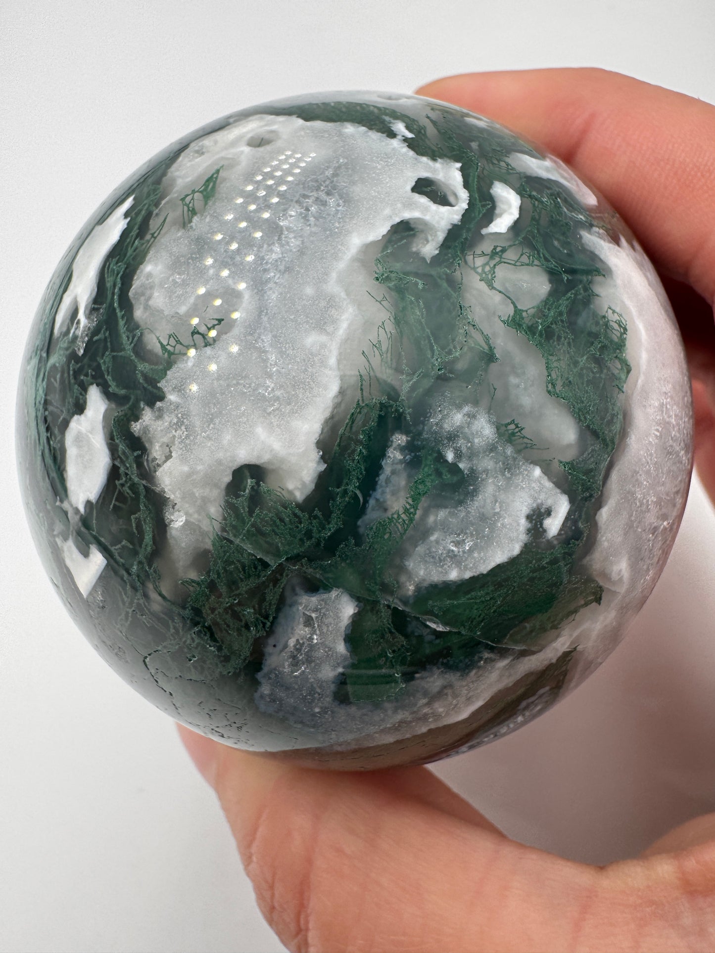 Eine hochglanzpolierte Moosachat-Kugel mit tiefgrünen, pflanzenähnlichen Strukturen in einer teils transparenten Matrix.