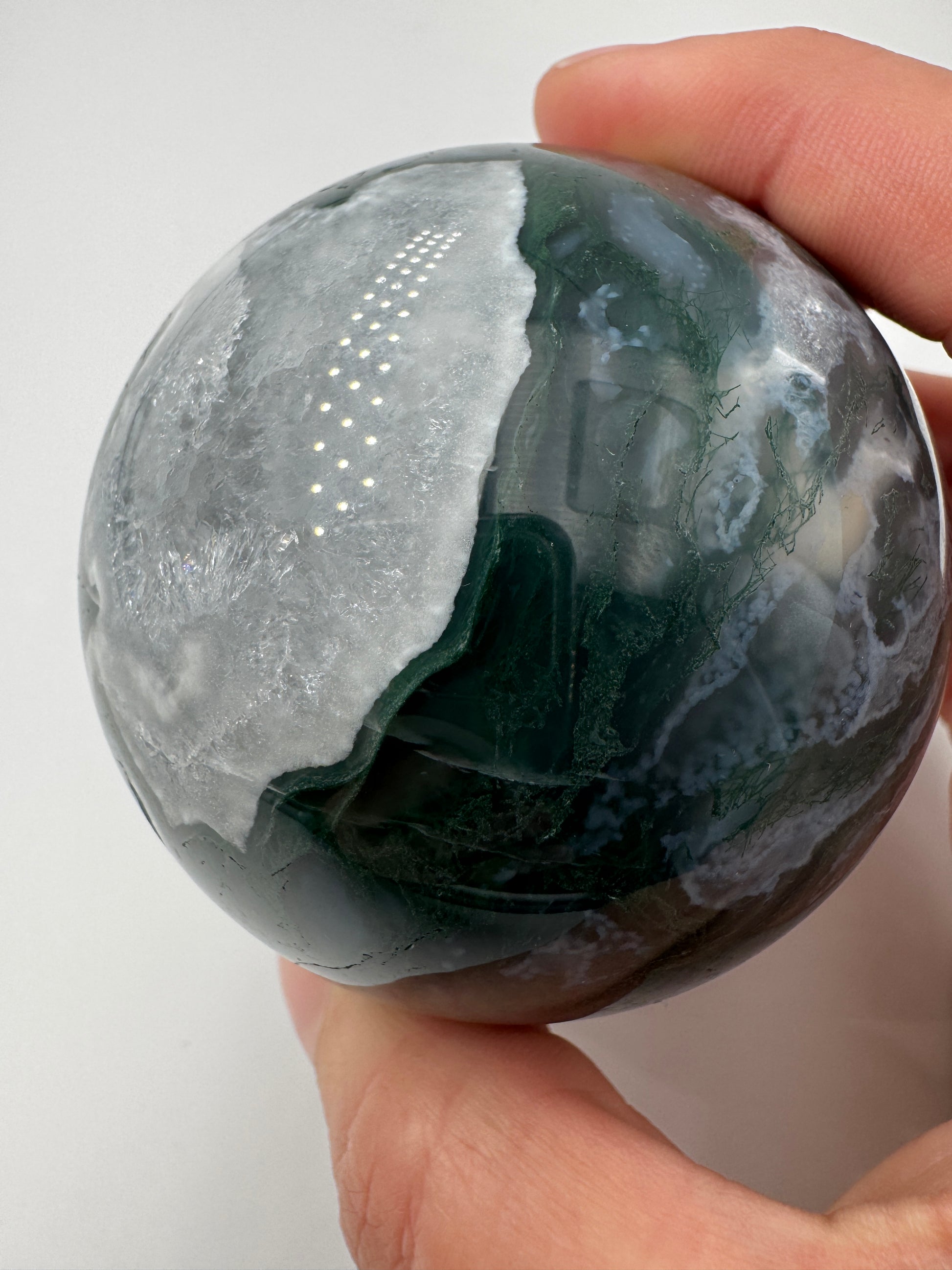 Eine hochglanzpolierte Moosachat-Kugel mit tiefgrünen, pflanzenähnlichen Strukturen in einer teils transparenten Matrix.