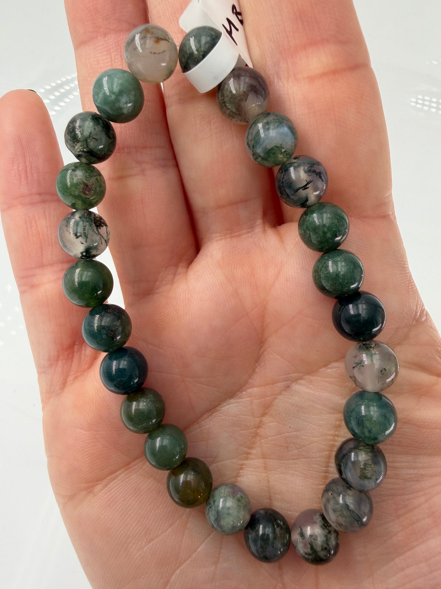 Ein hochwertiges Kugelarmband aus Moosachat, dessen einzelne Perlen klare bis weißliche Partien mit tiefgrünen Mineraleinschlüssen kombinieren.