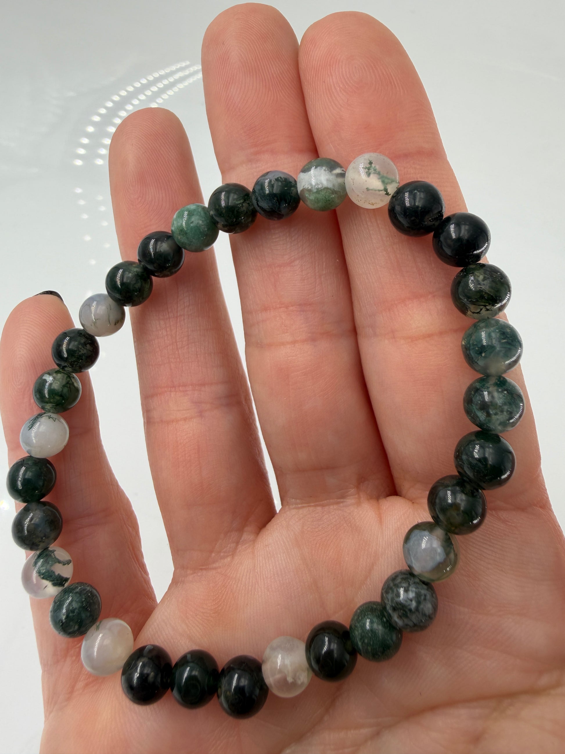 Ein hochwertiges Kugelarmband aus Moosachat, dessen einzelne Perlen klare bis weißliche Partien mit tiefgrünen Mineraleinschlüssen kombinieren.