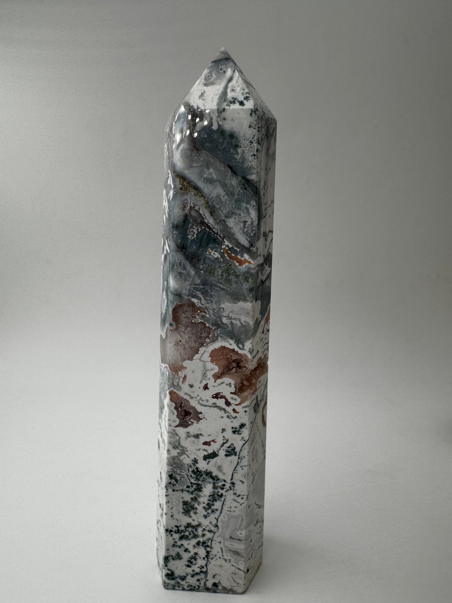 Ein präzise geschliffener Moosachat-Obelisk mit grünen Mustern und einer offenen, mit rosa Quarzkristallen.