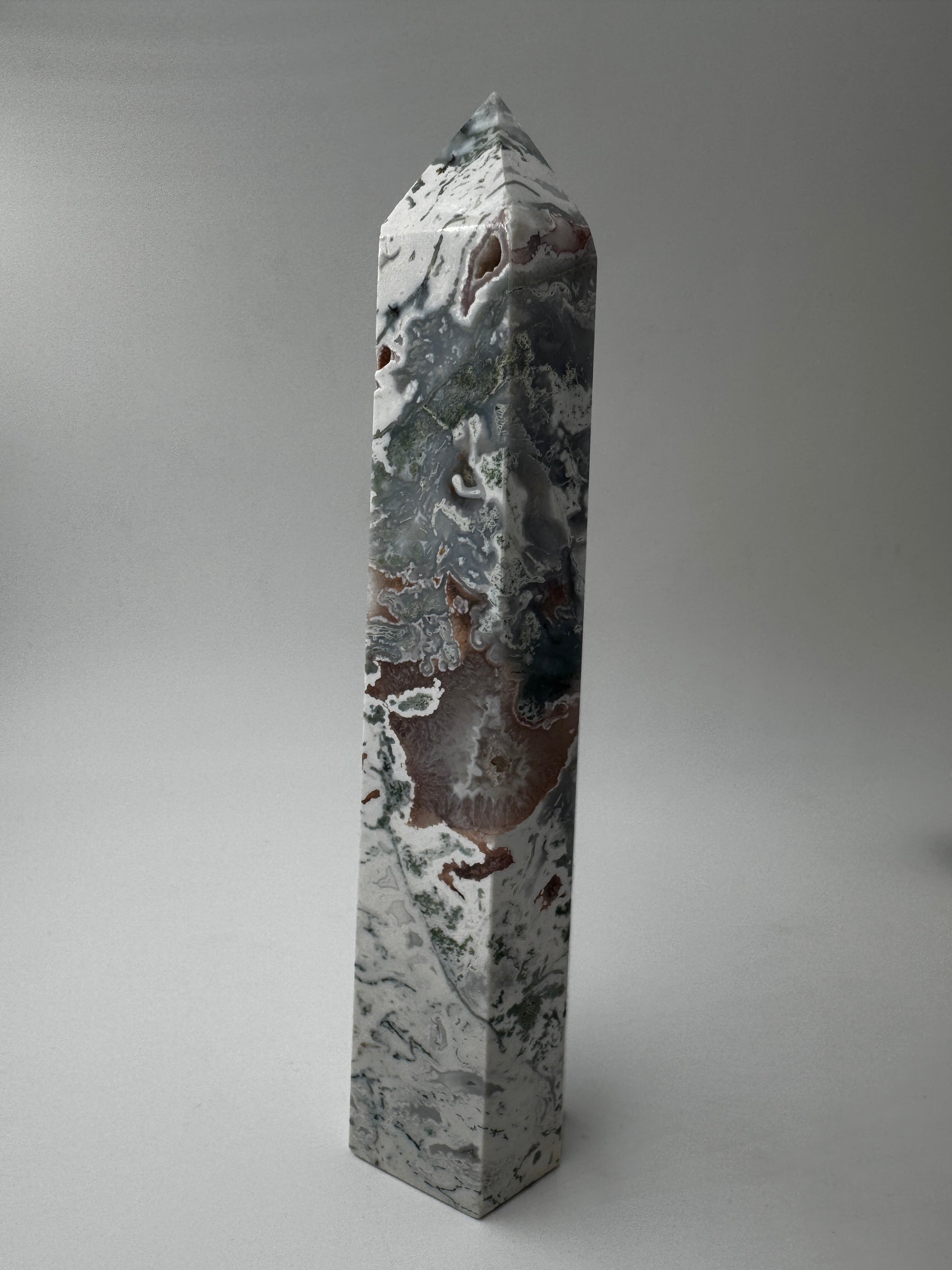 Ein präzise geschliffener Moosachat-Obelisk mit grünen Mustern und einer offenen, mit rosa Quarzkristallen.