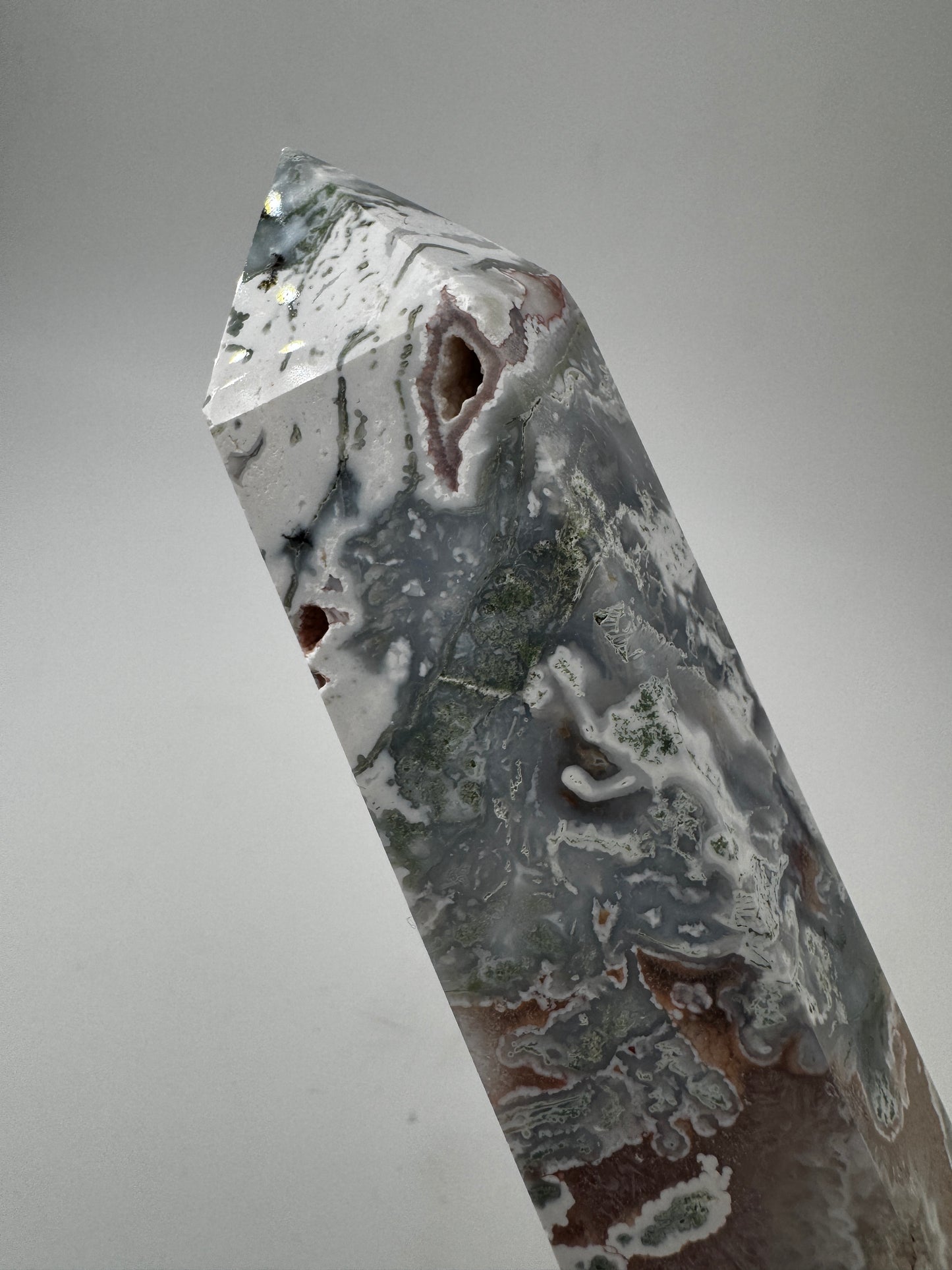Ein präzise geschliffener Moosachat-Obelisk mit grünen Mustern und einer offenen, mit rosa Quarzkristallen.