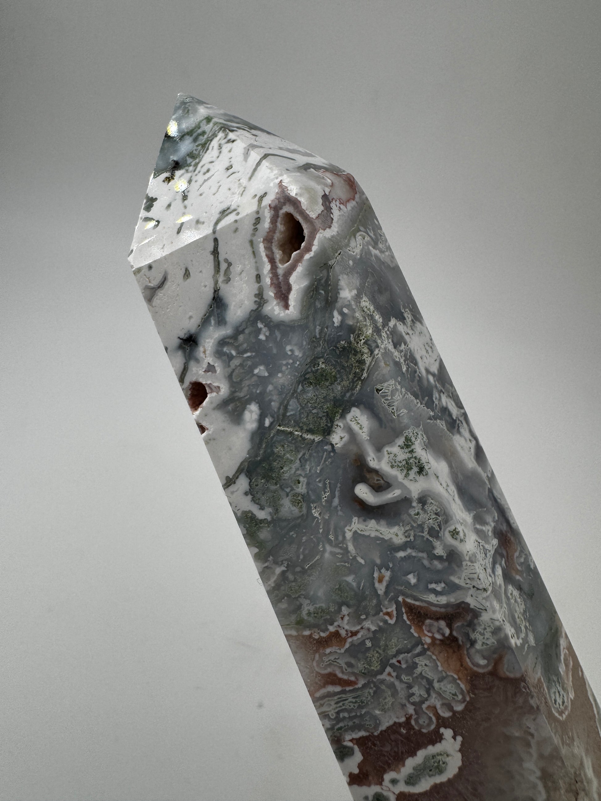 Ein präzise geschliffener Moosachat-Obelisk mit grünen Mustern und einer offenen, mit rosa Quarzkristallen.