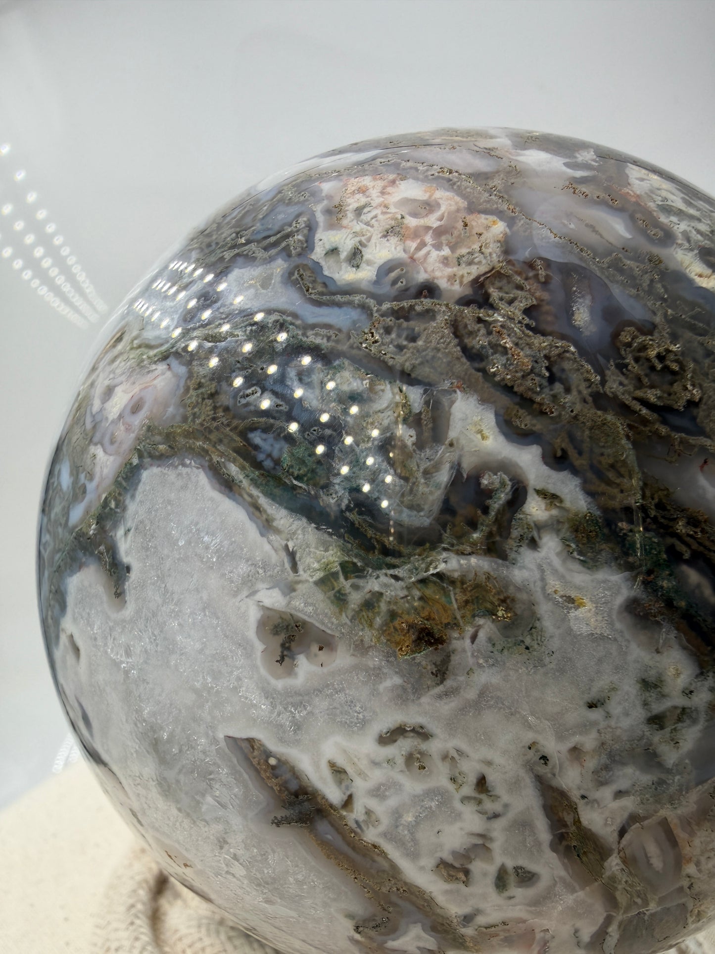 Eine hochglanzpolierte Moosachat-Kugel mit tiefgrünen, pflanzenähnlichen Strukturen in einer teils transparenten Matrix.