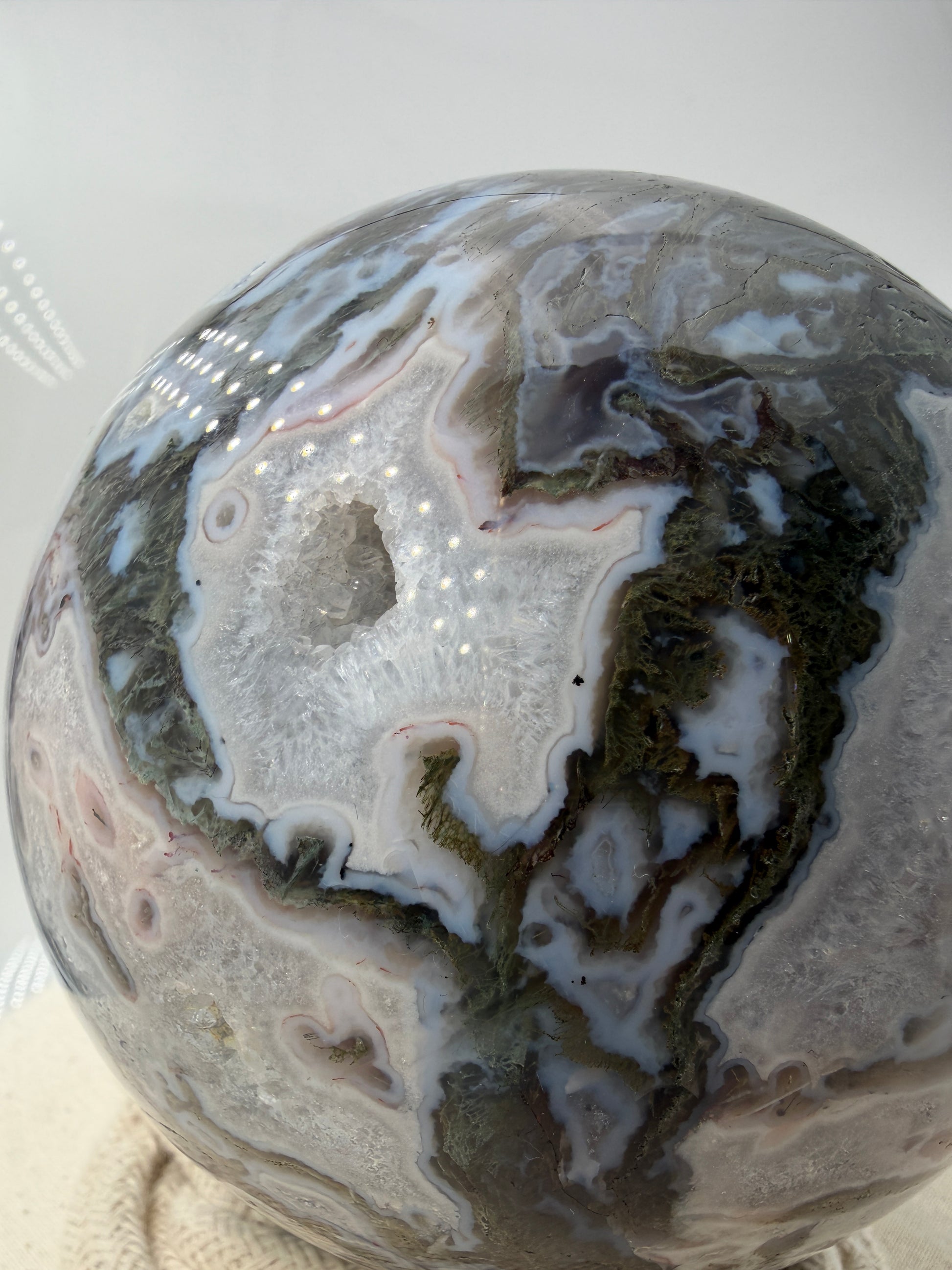 Eine hochglanzpolierte Moosachat-Kugel mit tiefgrünen, pflanzenähnlichen Strukturen in einer teils transparenten Matrix.