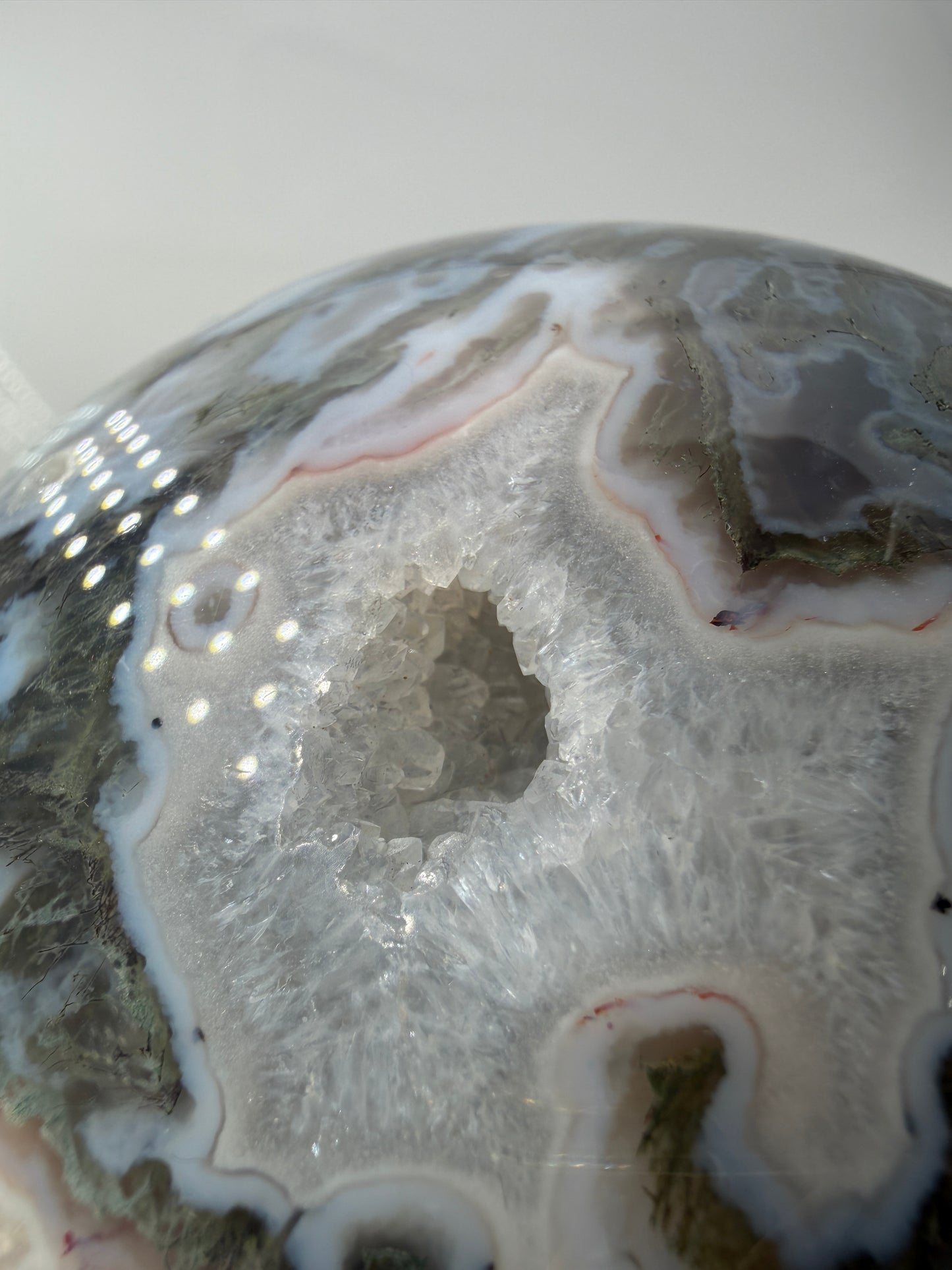 Eine hochglanzpolierte Moosachat-Kugel mit tiefgrünen, pflanzenähnlichen Strukturen in einer teils transparenten Matrix.