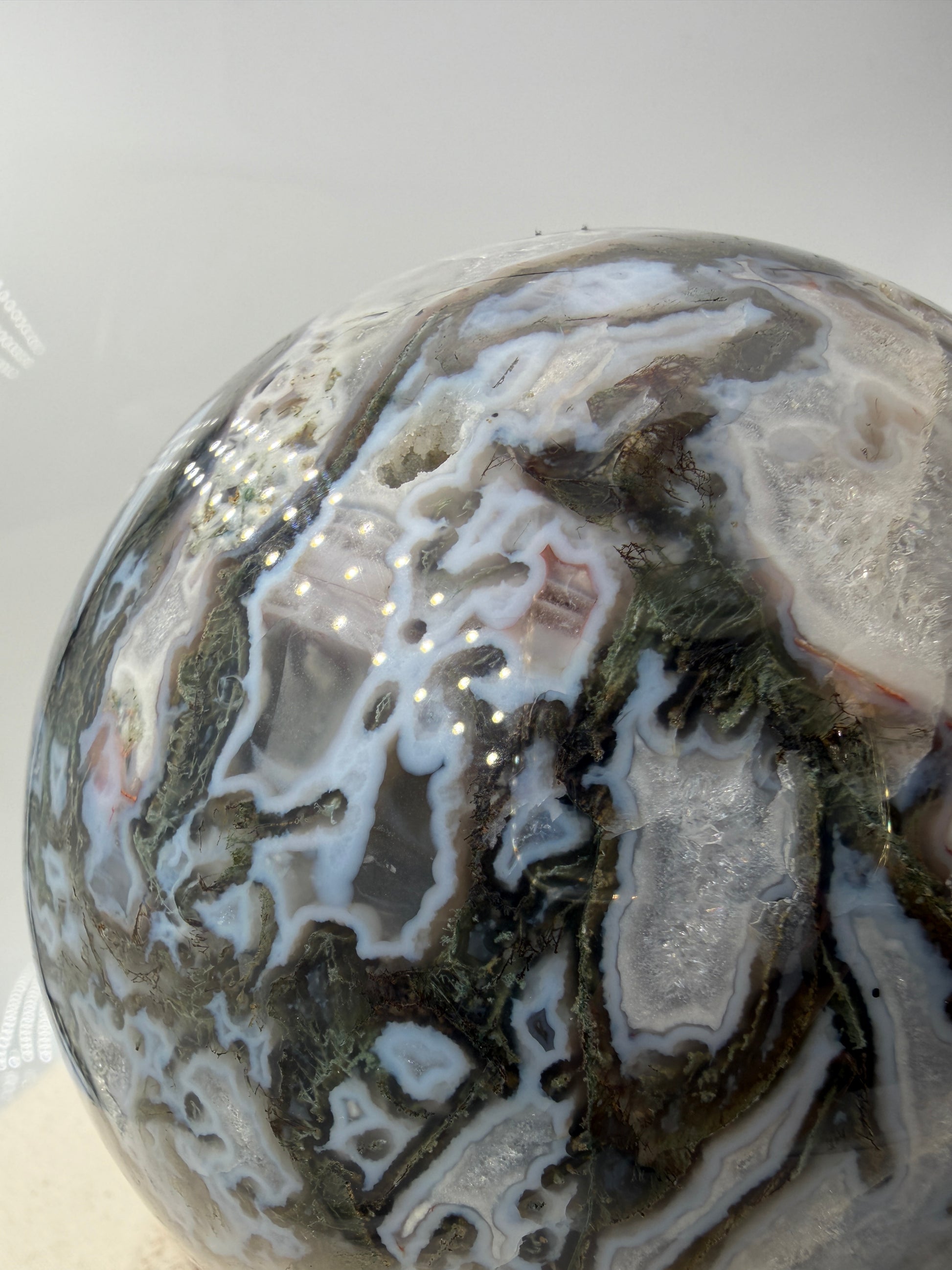 Eine hochglanzpolierte Moosachat-Kugel mit tiefgrünen, pflanzenähnlichen Strukturen in einer teils transparenten Matrix.