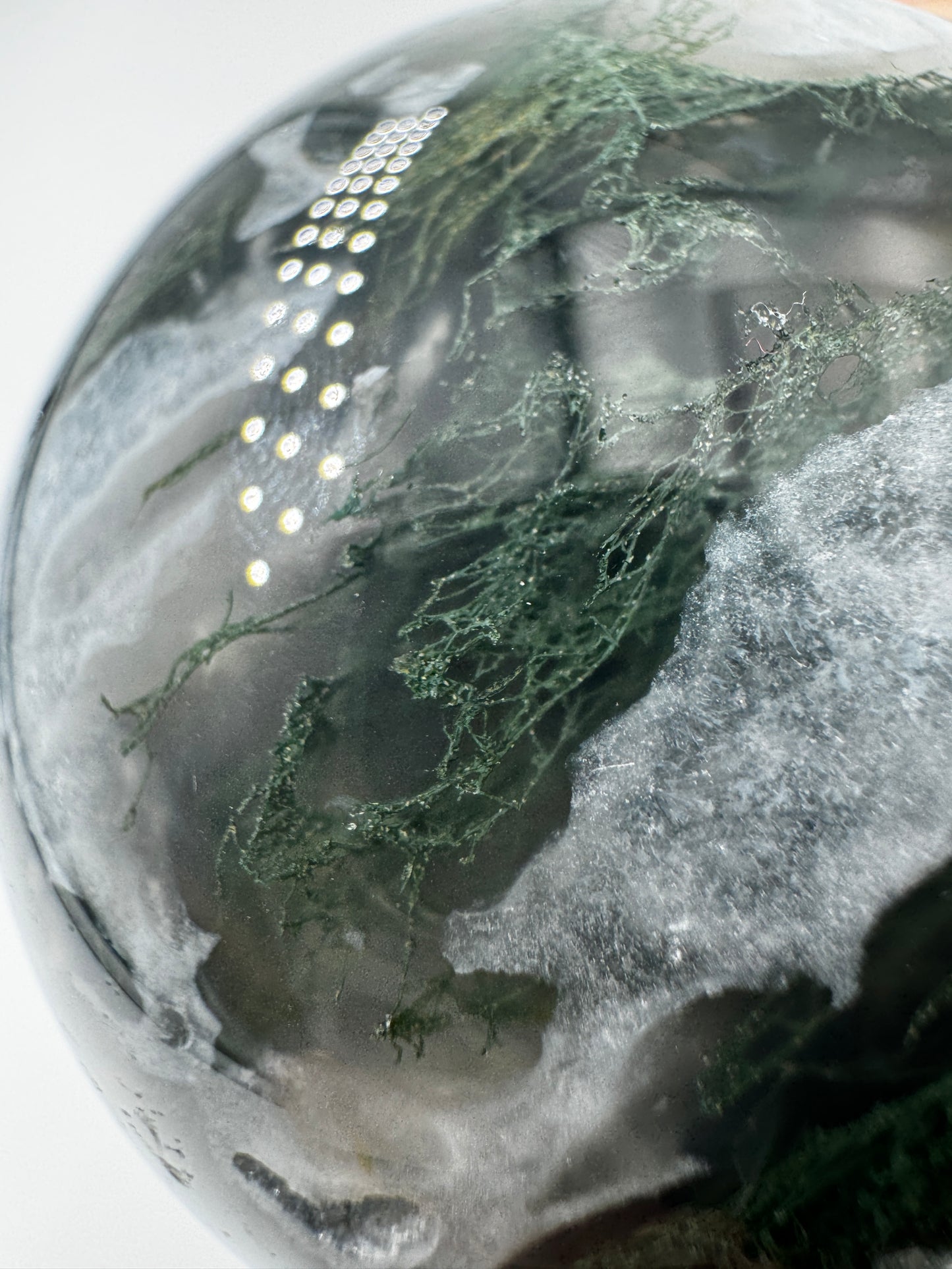 Eine hochglanzpolierte Moosachat-Kugel mit tiefgrünen, pflanzenähnlichen Strukturen in einer teils transparenten Matrix.