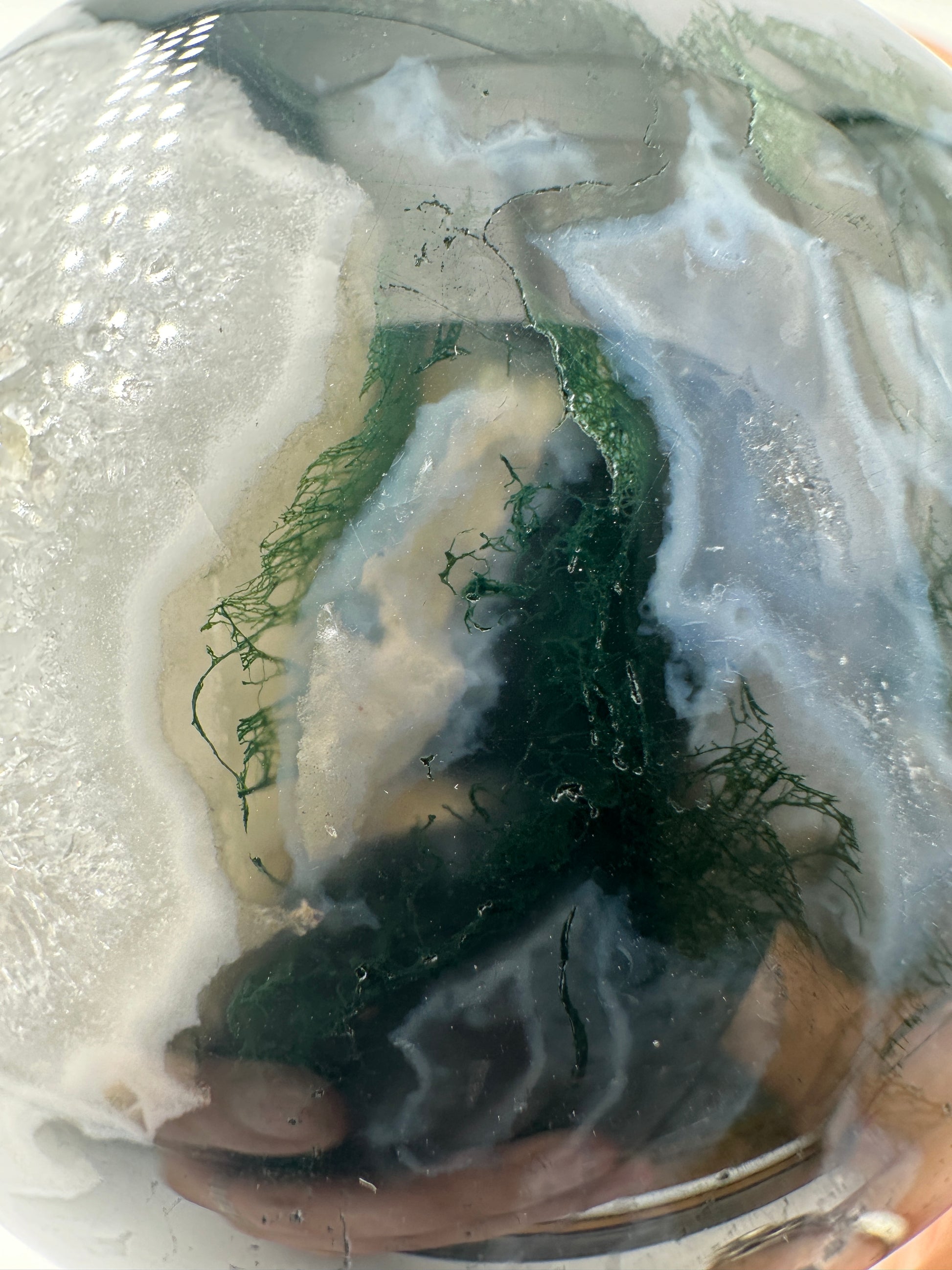 Eine auf hochglanzpolierte Moosachat-Kugel mit tiefgrünen, pflanzenähnlichen Strukturen in einer teils transparenten Matrix.