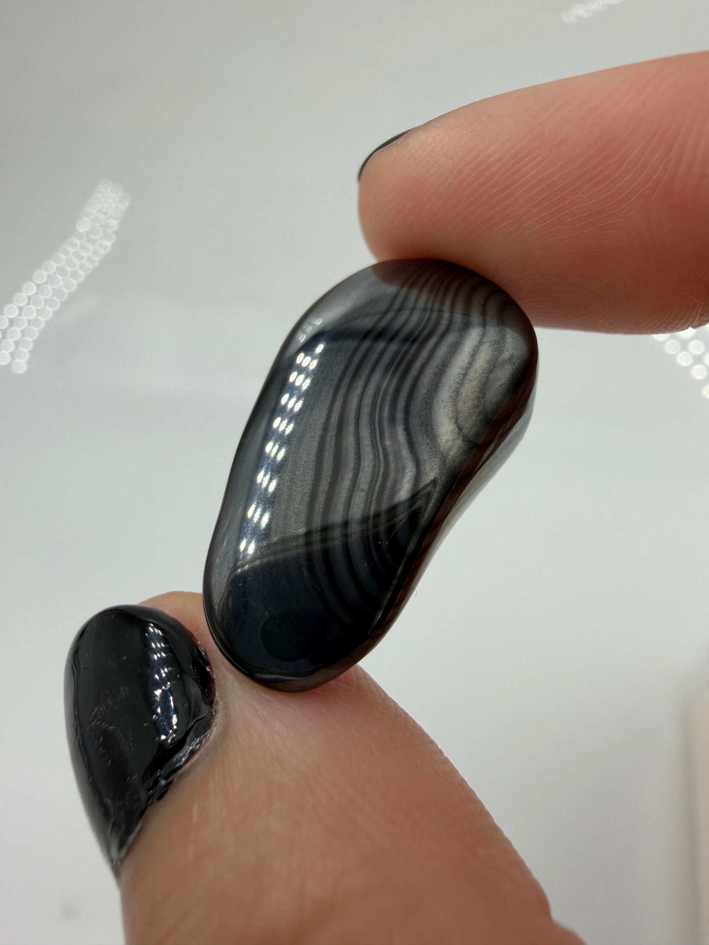 Tiefschwarze, metallisch glänzender Psilomelan-Trommelstein mit silbrig schimmernden, fließenden Linienstrukturen.