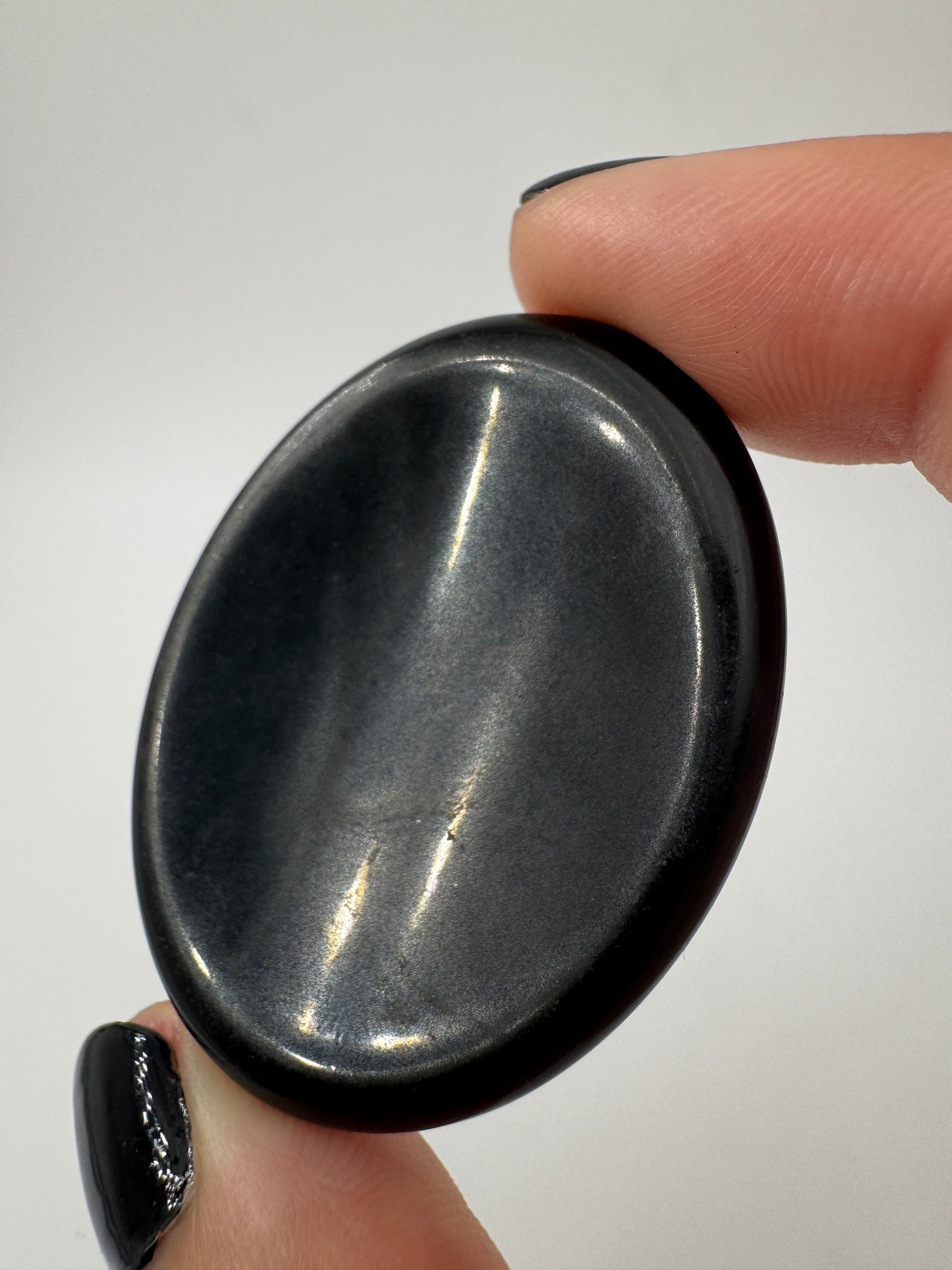 Ein  Daumensteinen aus Obsidian mit glänzend polierten Oberflächen und zentraler Daumenmulde.