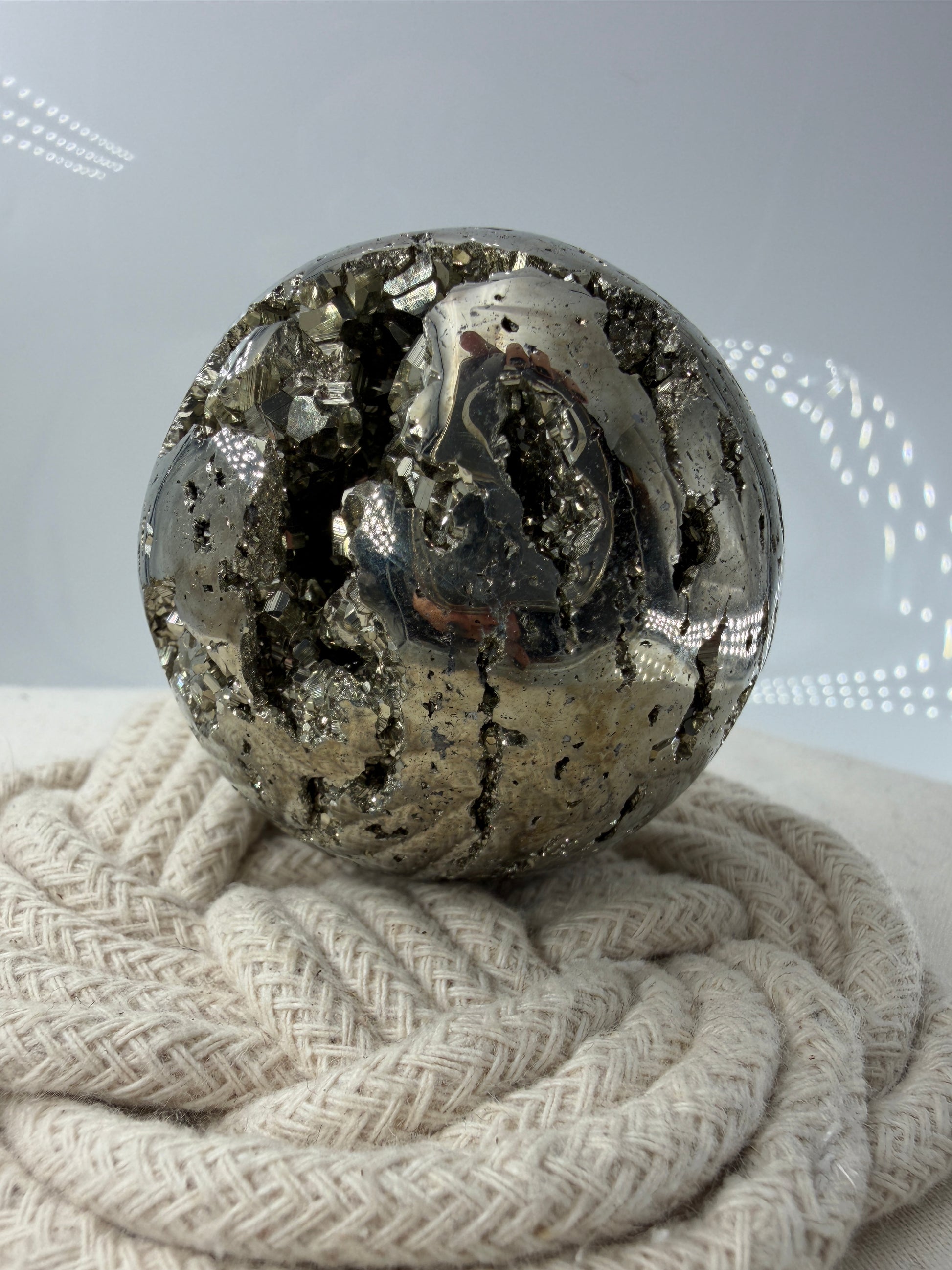 Eine hochglänzende, metallisch Pyrit-Kugel, deren spiegelnde Oberfläche die Umgebung reflektiert und winzige, natürliche Kristallstrukturen offenbart.